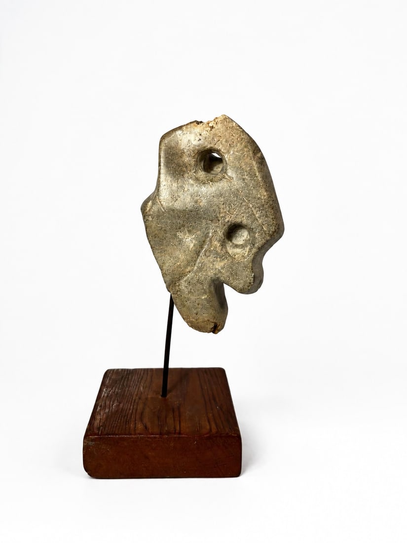 Stylized Pre-Columbian Anthropomorphic Stone Effigy: A compelling and heavily stylized carved stone hacha (ceremonial axe), hand-sculpted from a dense, granular volcanic stone matrix. The profile form mimics a stylized human head or zoomorphic profile c