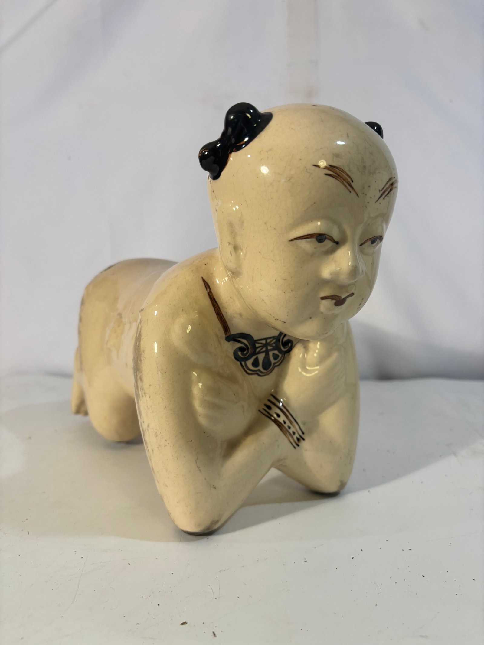 A Chinese Cizhou Porcelain Pillow: The item is an antique Chinese porcelain pillow shaped like a kneeling boy. It features a cream or yellowish-white crackle glaze with brown or black accents on the hair, facial features, and jewelry. 
