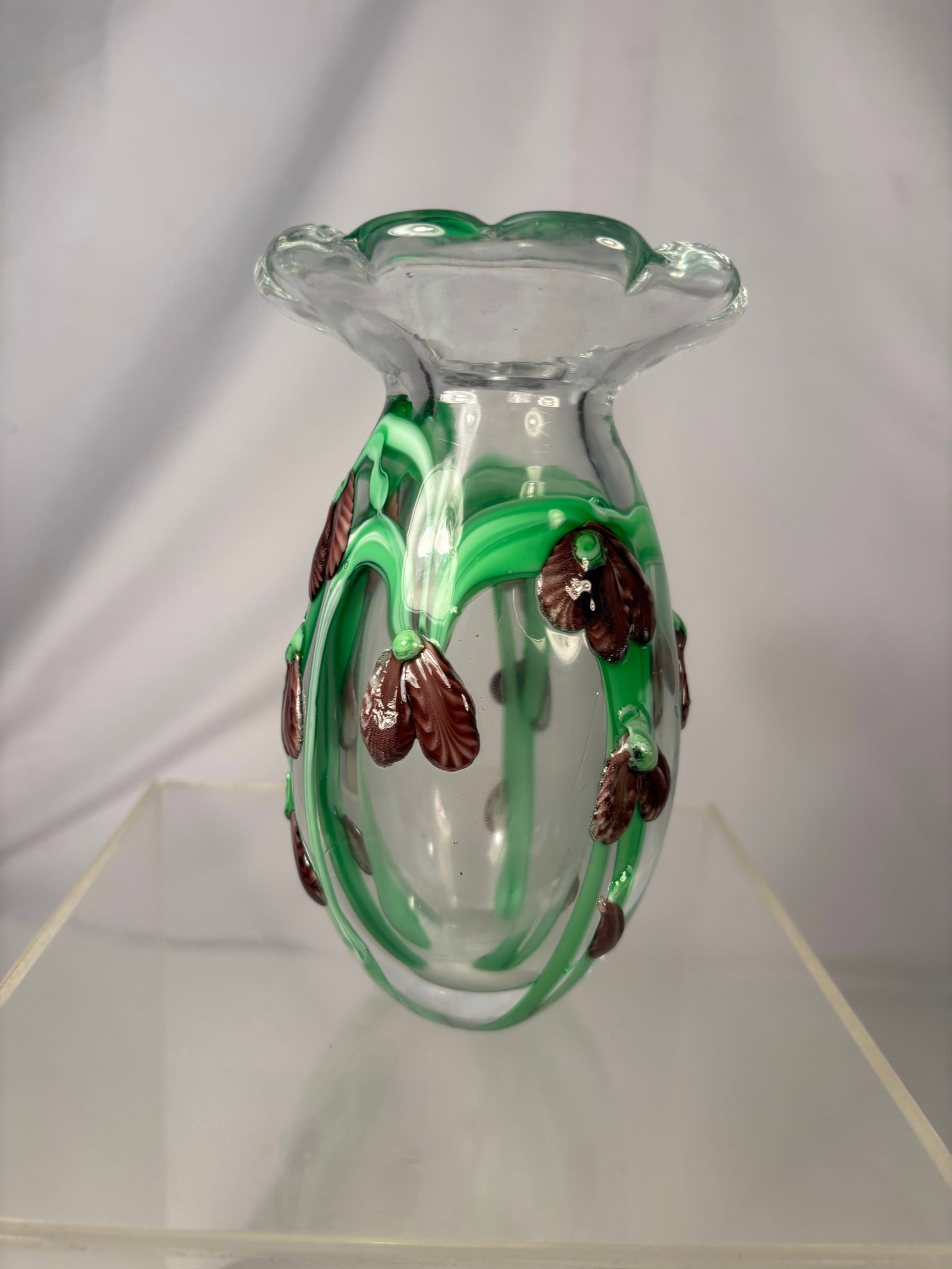 Vintage Murano-style art Glass Vase with Applied Floral Decoration: A decorative hand-blown clear art glass vase featuring an organic ruffled rim, vibrant green applied glass vines, and burgundy flower-form accents. The rounded body rests on a thick glass base with a 