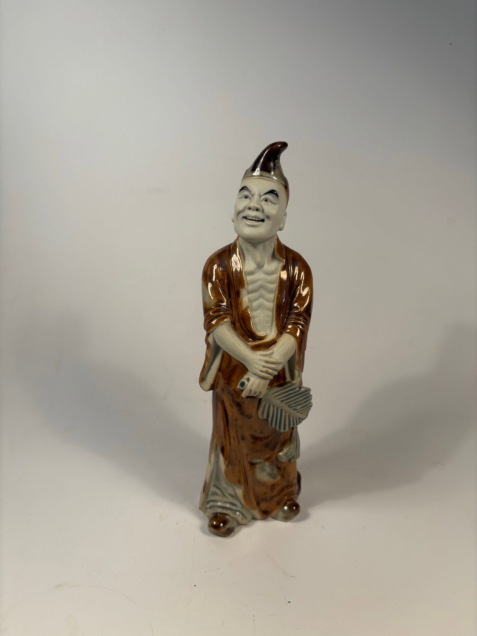 A Chinese Famille rose procelain statue: Qing Dynasty (1644-1912); figure of a smiling man holding a folding fan, dressed in a flowing robe with detailed facial features and expressive posture.Dimensions?Height: 9 inches.