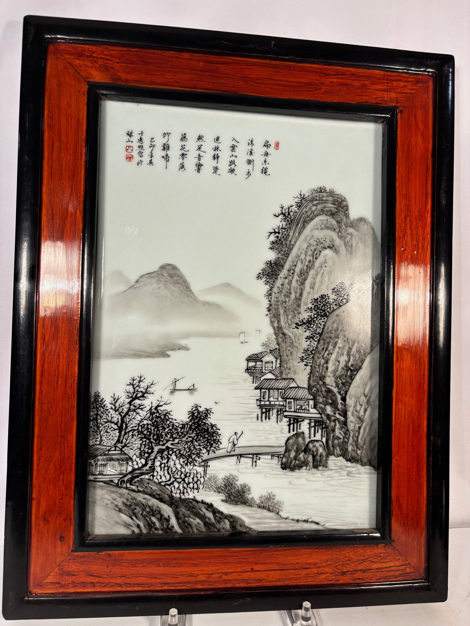 A Chinese Framed Porcelain Plaque with Ink Landscape and Calligraphy Signed and dated: A Chinese porcelain plaque finely painted in monochrome ink style, depicting a tranquil mountainous riverside landscape with scholars’ dwellings, pavilions, mist-shrouded water, and distant peaks. T