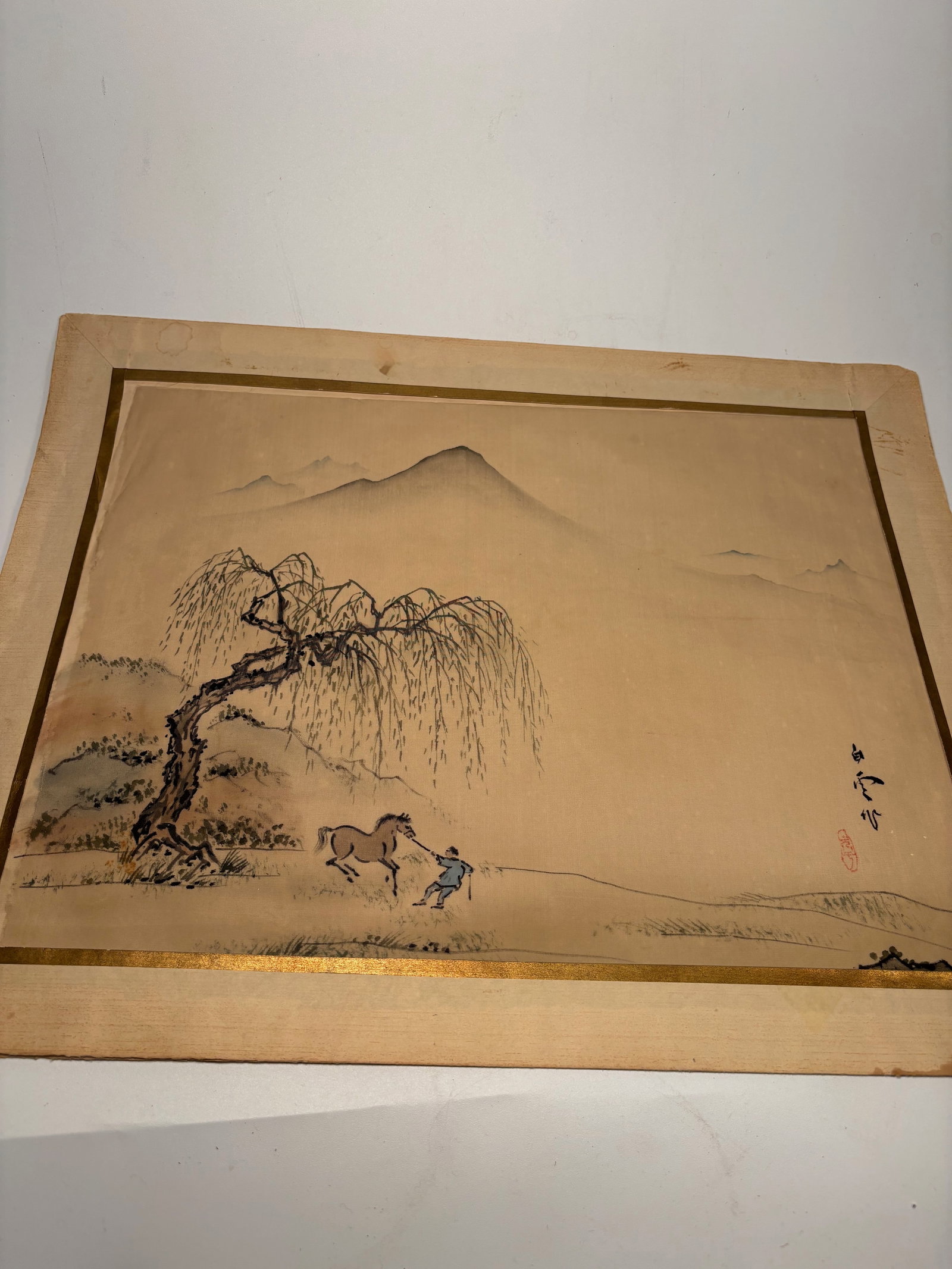 A Japanese Nihonga Watercolor on Silk, Signed Hakuun: 19th century;A delicate Japanese watercolor on silk depicting a poetic rural landscape with a bent willow tree and a young figure guiding a horse across an open field. In the distance, misty mountain 