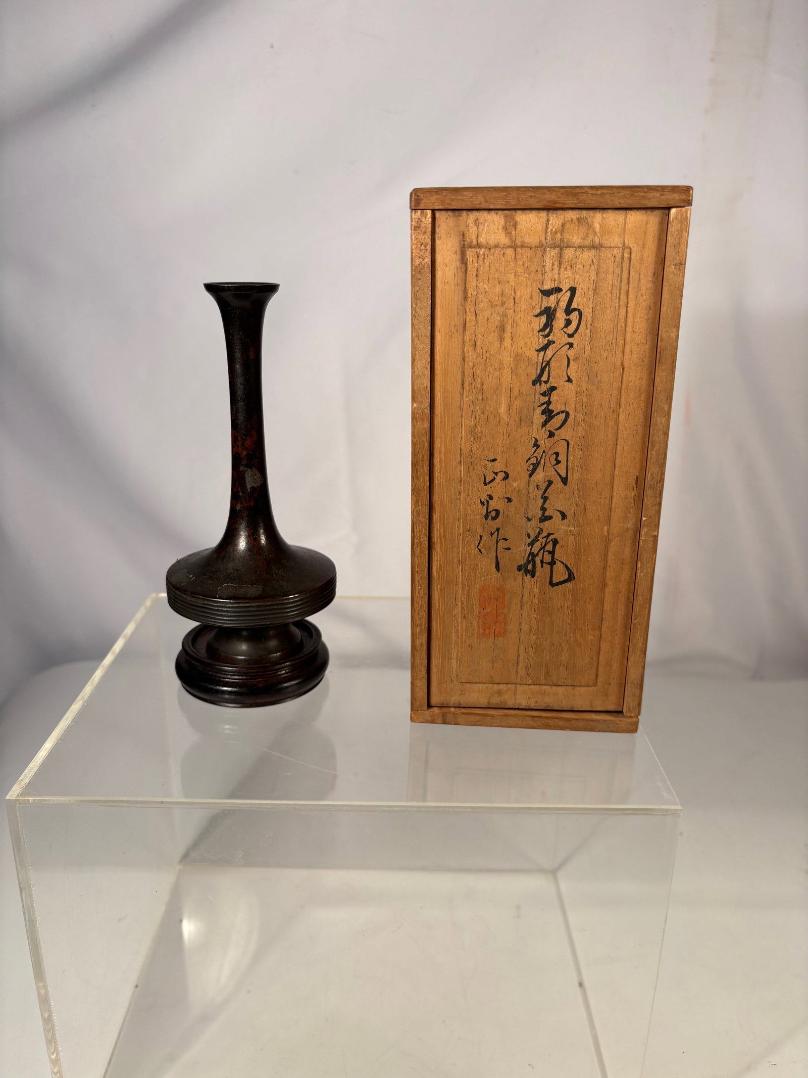 A Japanese Bronze Ikebana Vase, Issan, with Original Tomobako Box, Meiji period (1868–1912).: Japanese patinated bronze ikebana vase of slender form with flared mouth and stepped base, accompanied by its original tomobako box inscribed “Bronze Flower Vase, made by Issan.” Japan, Meiji 