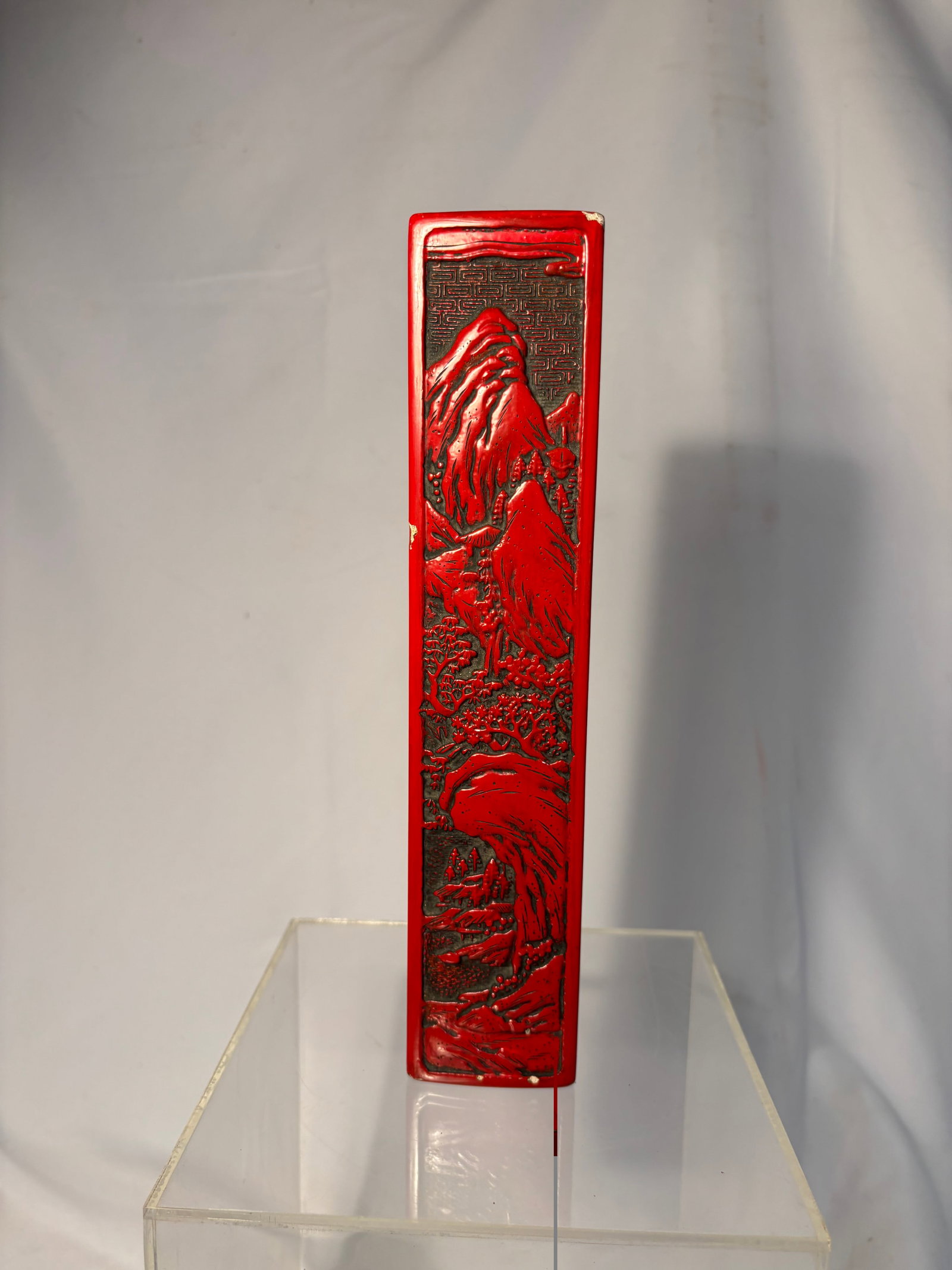 A Japanese Red Lacquer Carved Brush Case / Suzuribako Style Scholar’s Box: A Japanese red lacquer carved scholar’s brush case or pen box, decorated in relief with mountainous landscape scenery, trees, and figures in traditional style. The rectangular fitted form is bordere