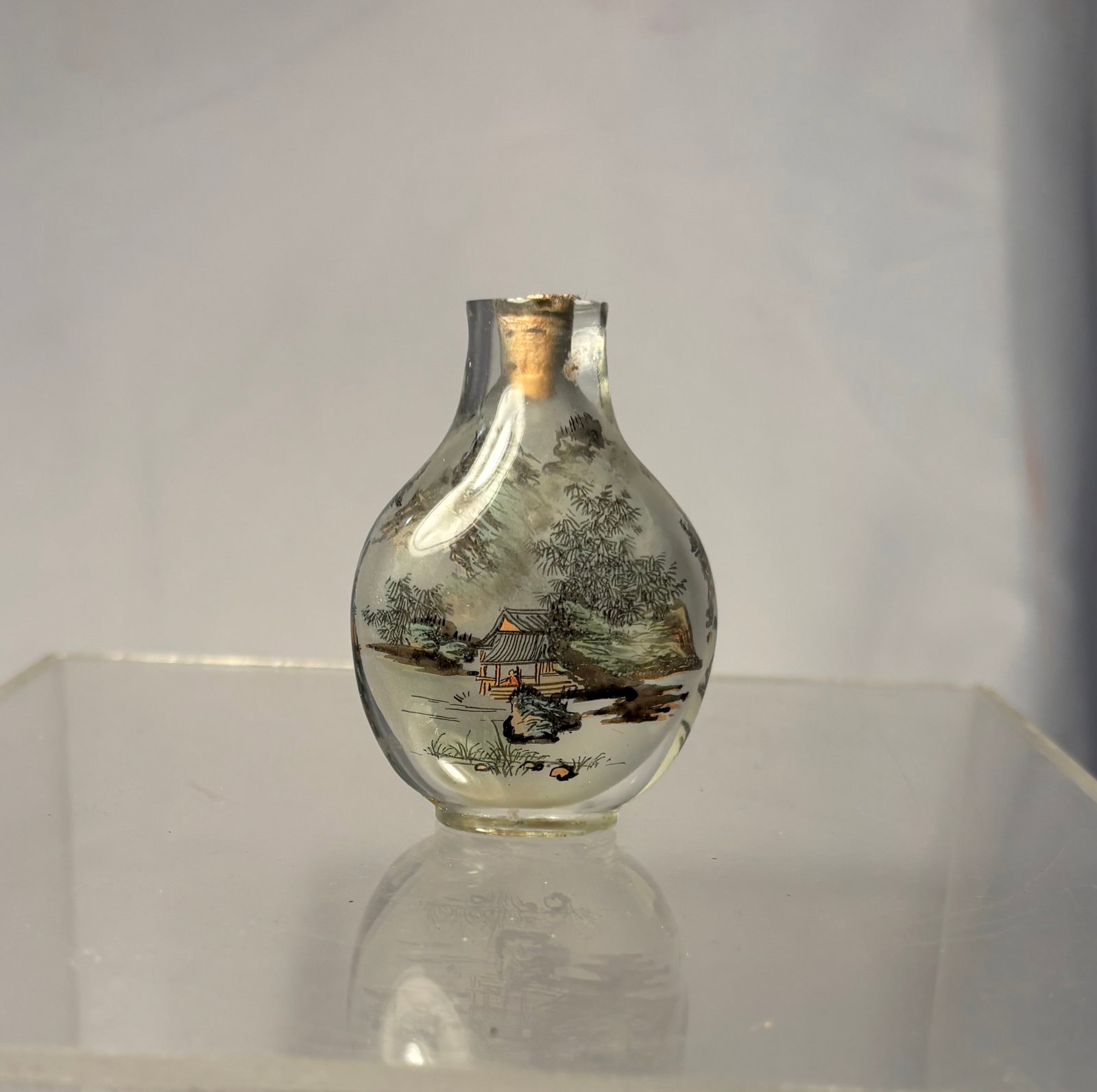 Chinese Inside Painted Glass Snuff Bottle Decorated with Scholar’s Landscape Scene signed: Early 20th century. A Chinese inside-painted snuff bottle featuring a finely executed mountain landscape scene with scholar’s pavilion, bamboo grove, and distant peaks. The translucent body is delic