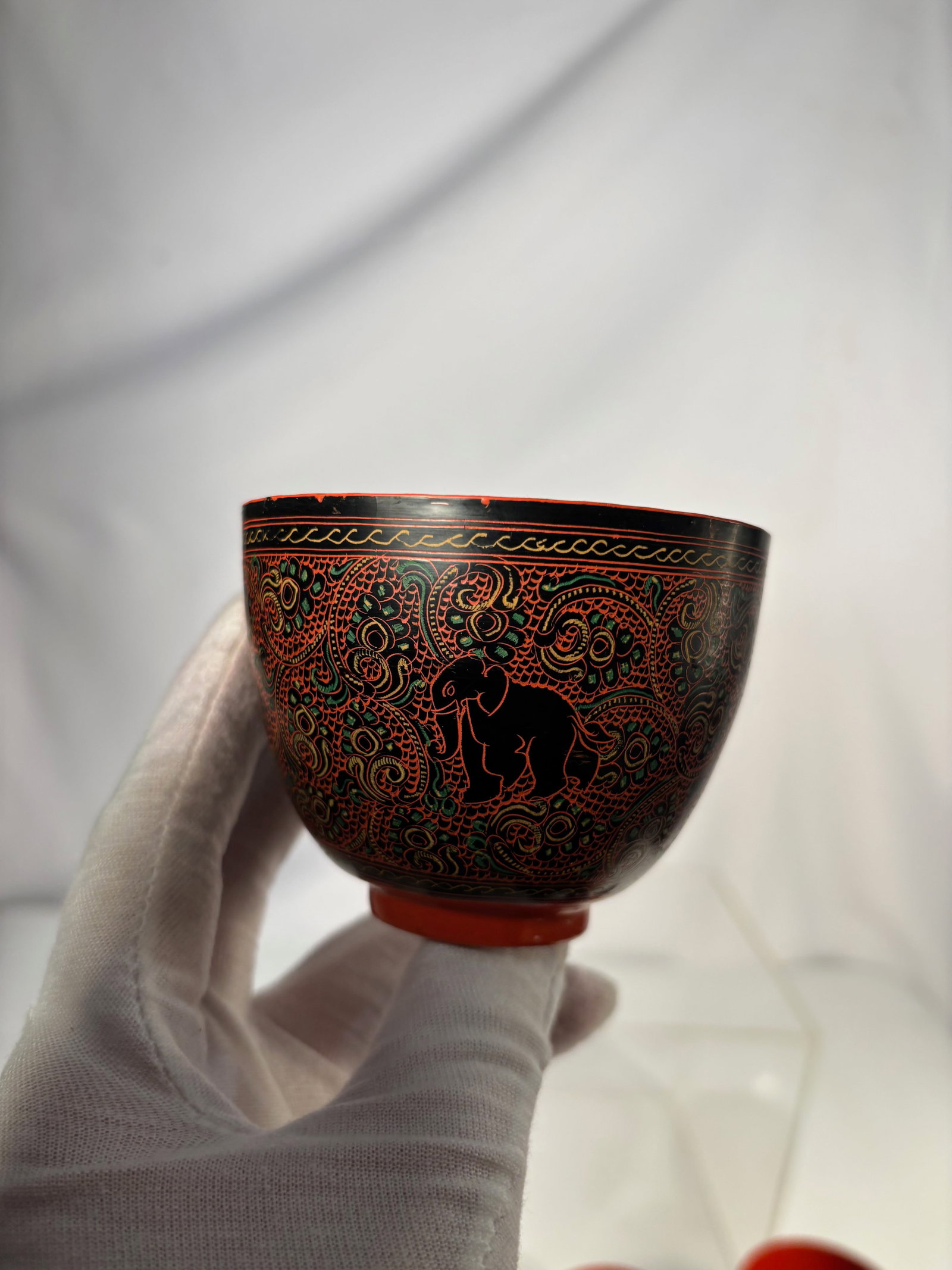 A Burmese Lacquerware Bowl with Elephant and Scrolling Decoration: A Burmese lacquerware bowl decorated with a stylized elephant set amid dense scrolling and foliate patterns, executed in red, green, and black on a dark ground. The exterior features finely incised an