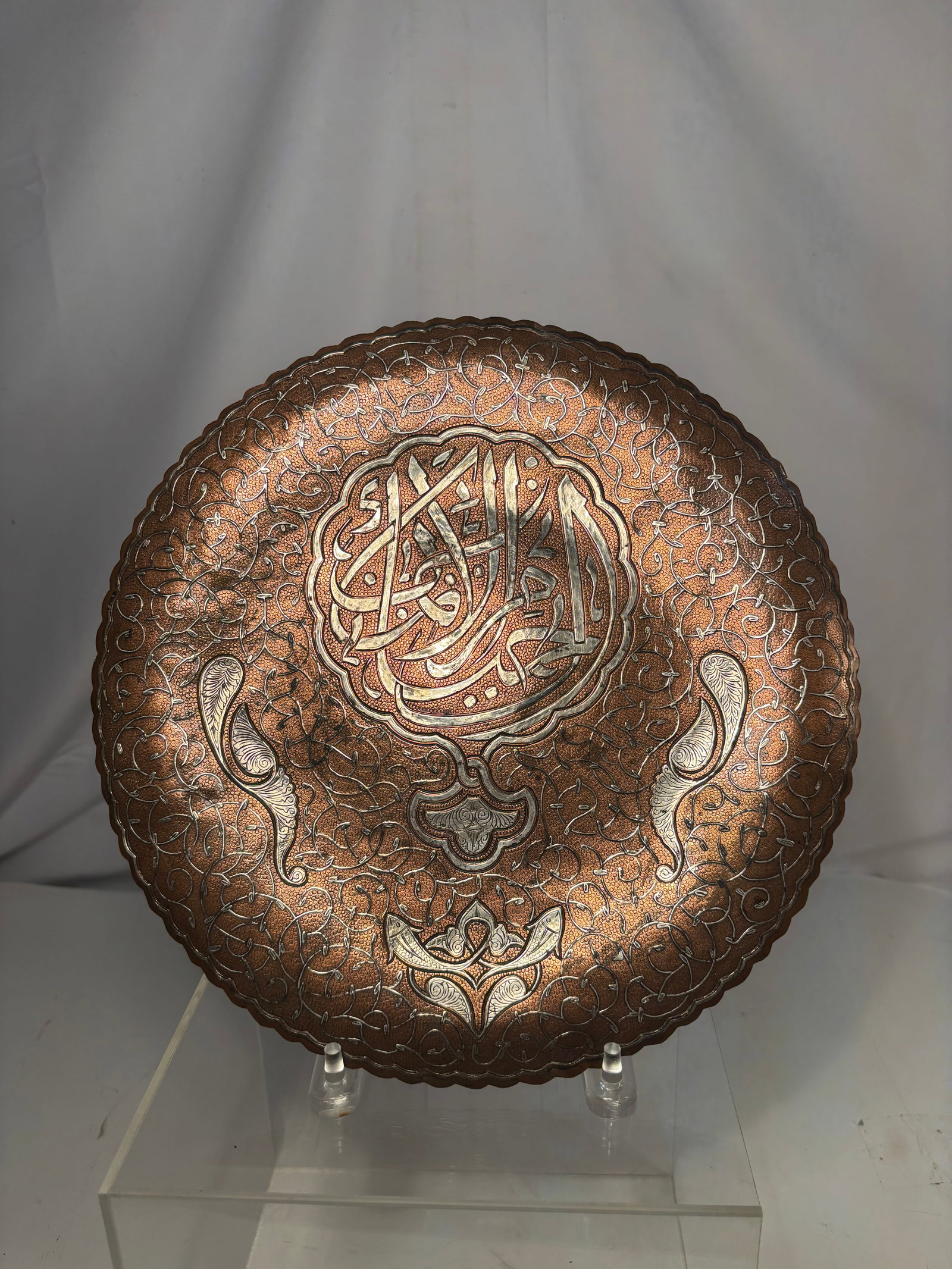 Islamic Mamluk Revival Silver-Inlaid Brass Calligraphic Tray , circa 1880–1920.: A large circular Middle Eastern brass tray or low tabletop, finely engraved with dense scrolling arabesques and silver-toned metal inlay. The central medallion contains bold Arabic calligraphy, surrou