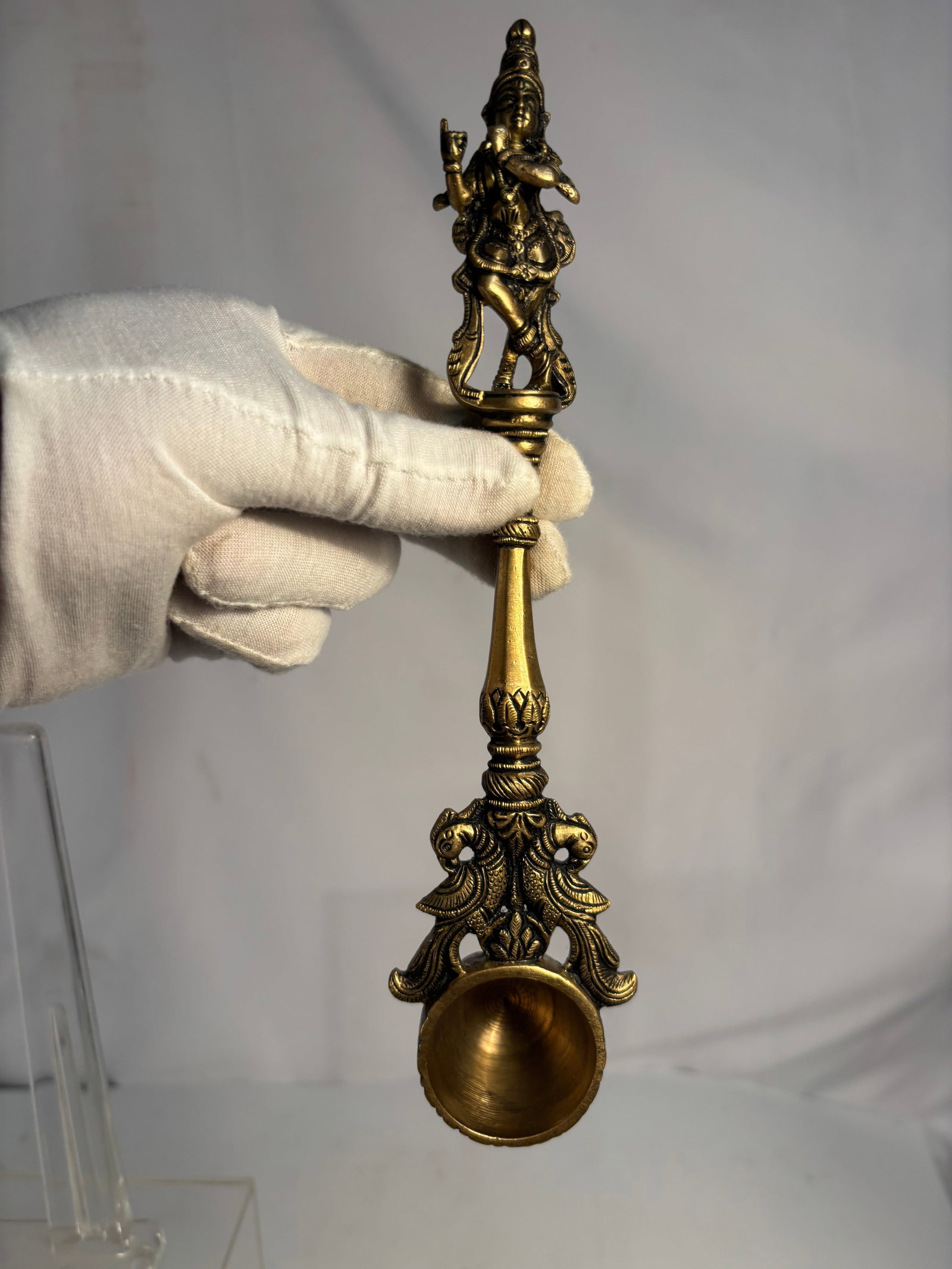 Vintage Indian Brass Krishna Hindu Ritual Puja Spoon: A vintage Indian cast-brass ritual spoon or ladle, traditionally used during Hindu puja or havan ceremonies for presenting offerings. The long, elaborately decorated handle is surmounted by a standing