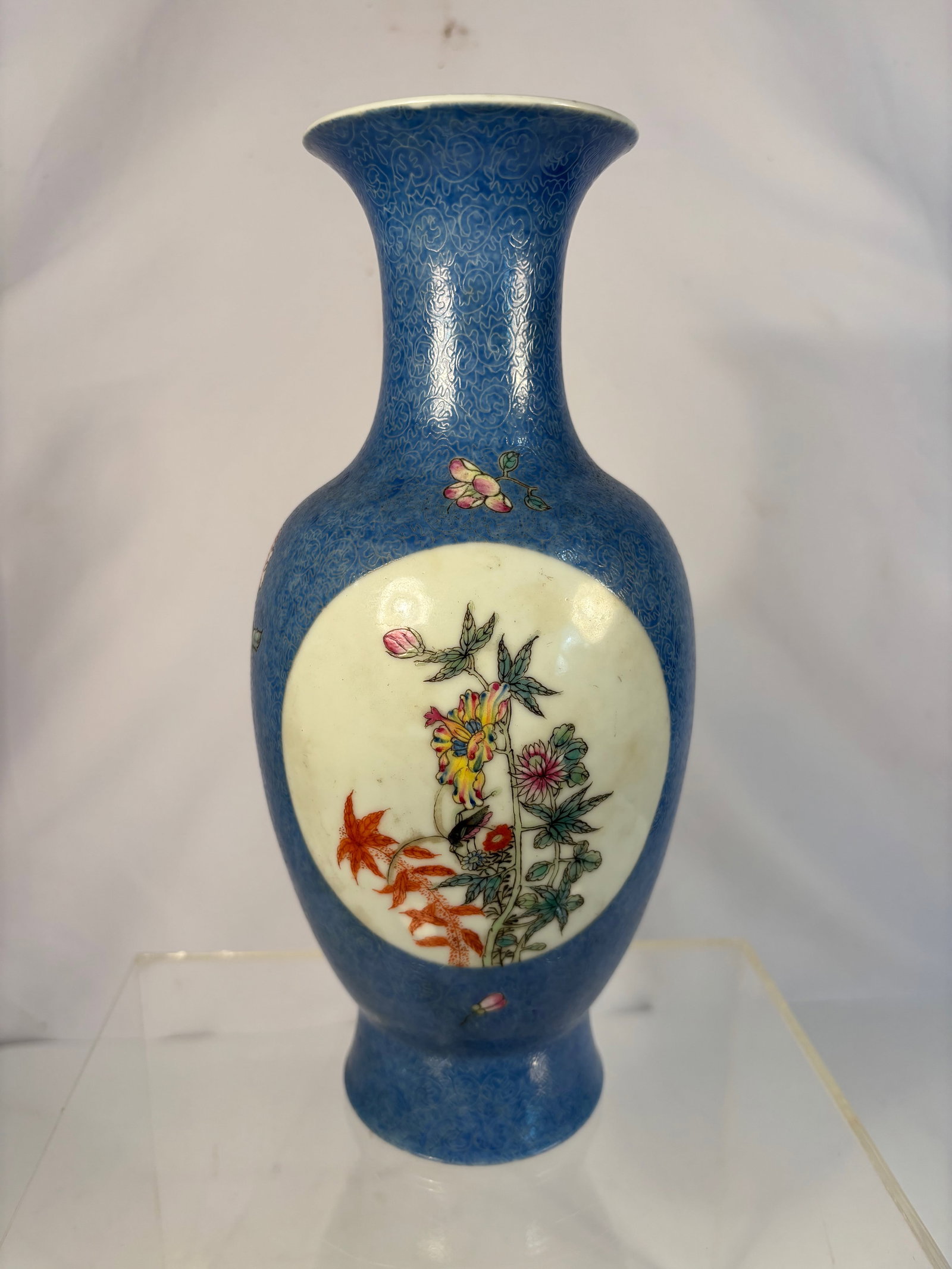 A Chinese Blue-Ground Famille Rose Vase, Qianlong Mark, Late 19th century to Early 20th century: Of baluster form with a flared neck, the body covered in a rich cobalt-blue enamel ground finely decorated with famille rose floral motifs and two white oval reserves painted with multicolored birds a
