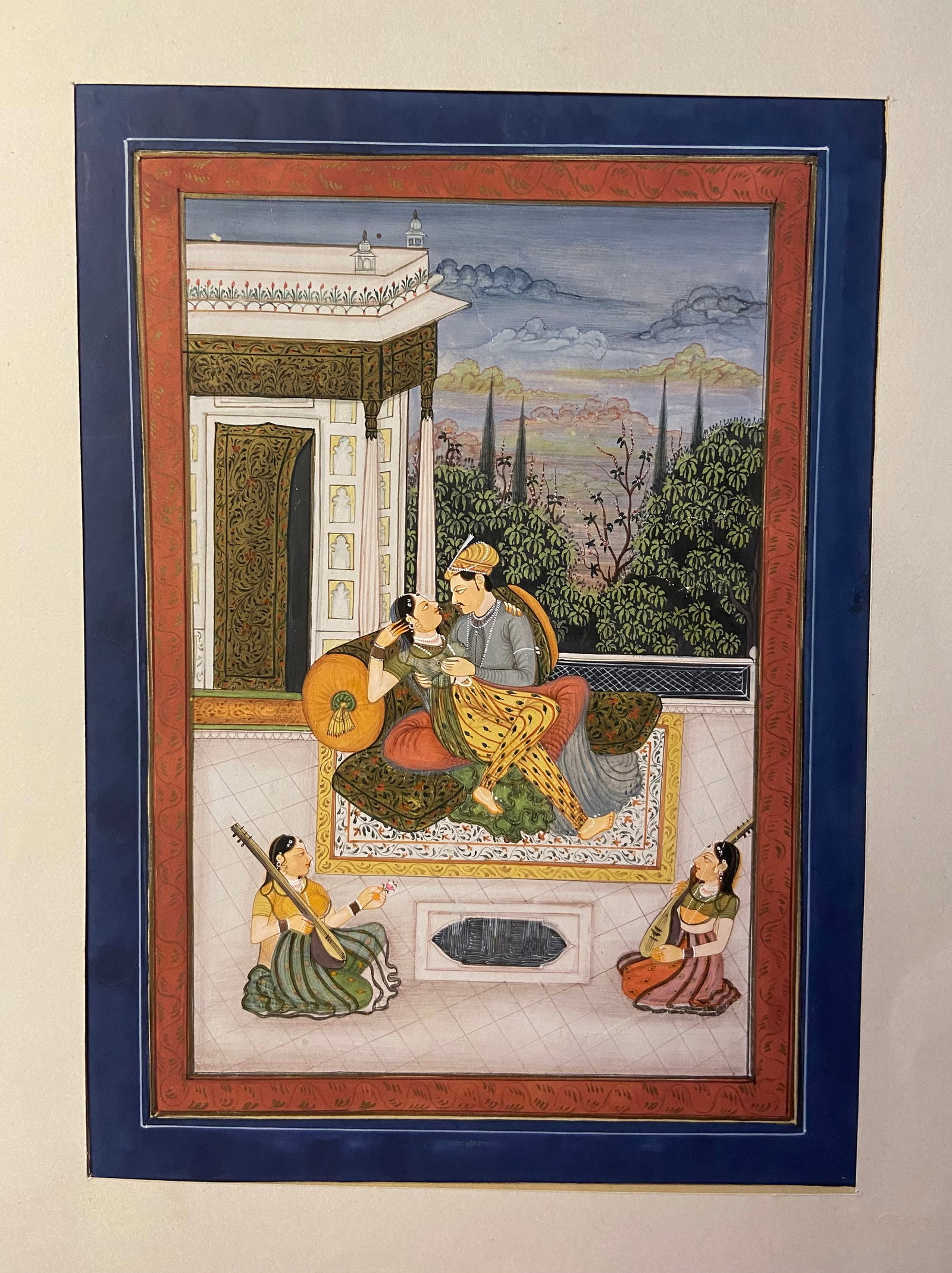 Indian Mughal Gouache Miniature of a Royal Couple with Court Musicians: 19th century; Indian Mughal miniature painting on paper, depicting a royal couple seated on a palace terrace in an intimate embrace. The pair is richly adorned with jewels and fine garments, with atte