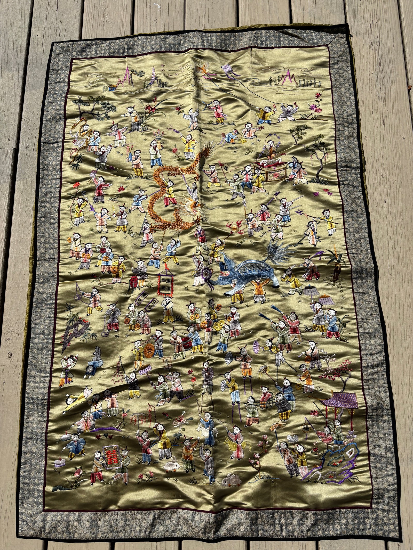 A Chinese embroidered silk panel: (c.1900–1930); Worked in vibrant silk threads on a golden silk ground, depicting numerous children (???) engaged in festive activities, including playing instruments, carrying banners and lanterns, 