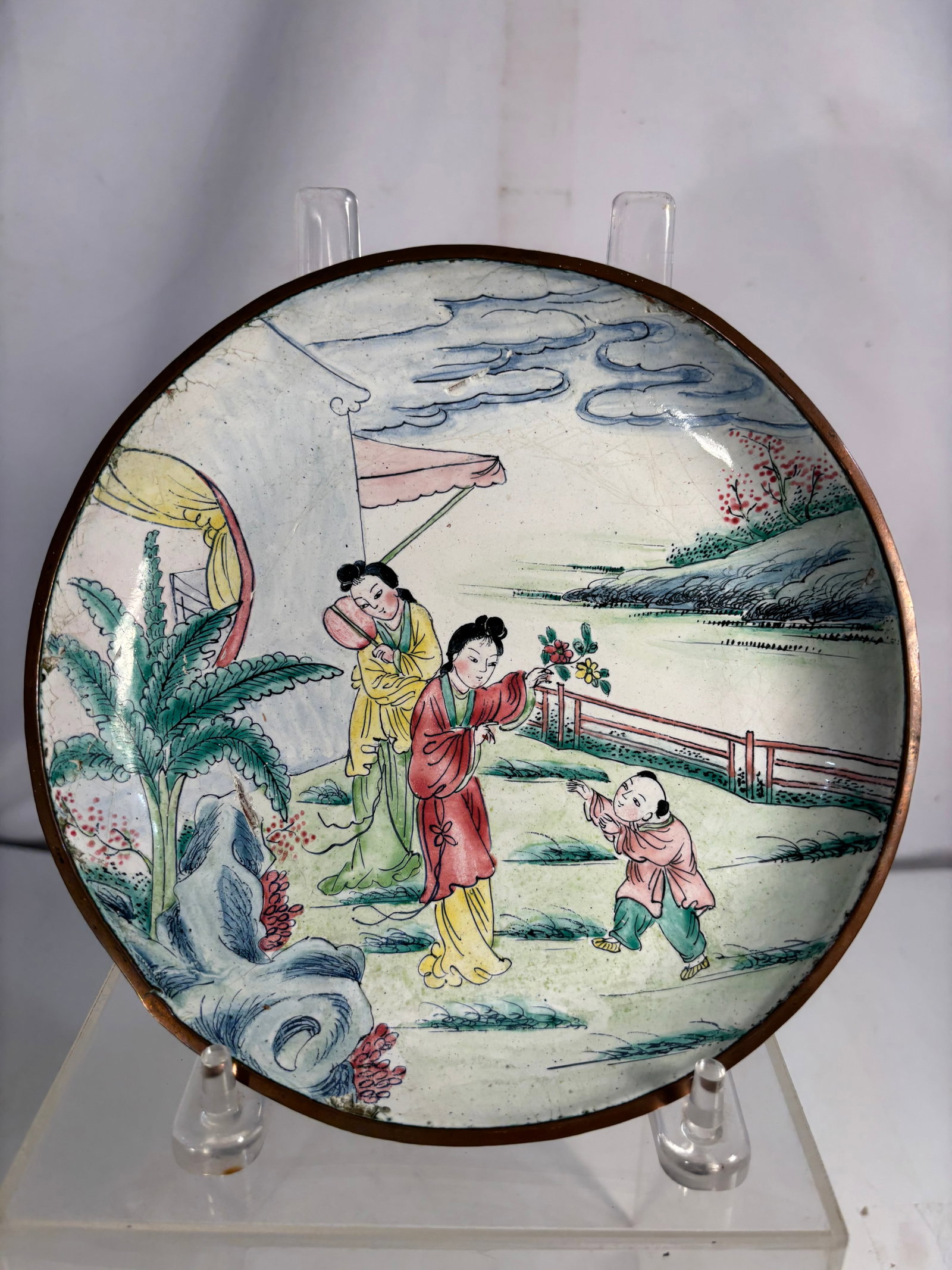 Chinese Enameled Copper Charger with Courtyard Figures, Qianlong Mark: Chinese painted enamel on copper charger decorated with an elegant courtyard scene depicting ladies and a child in a landscaped garden. The reverse bears a four-character iron-red Qianlong mark, which