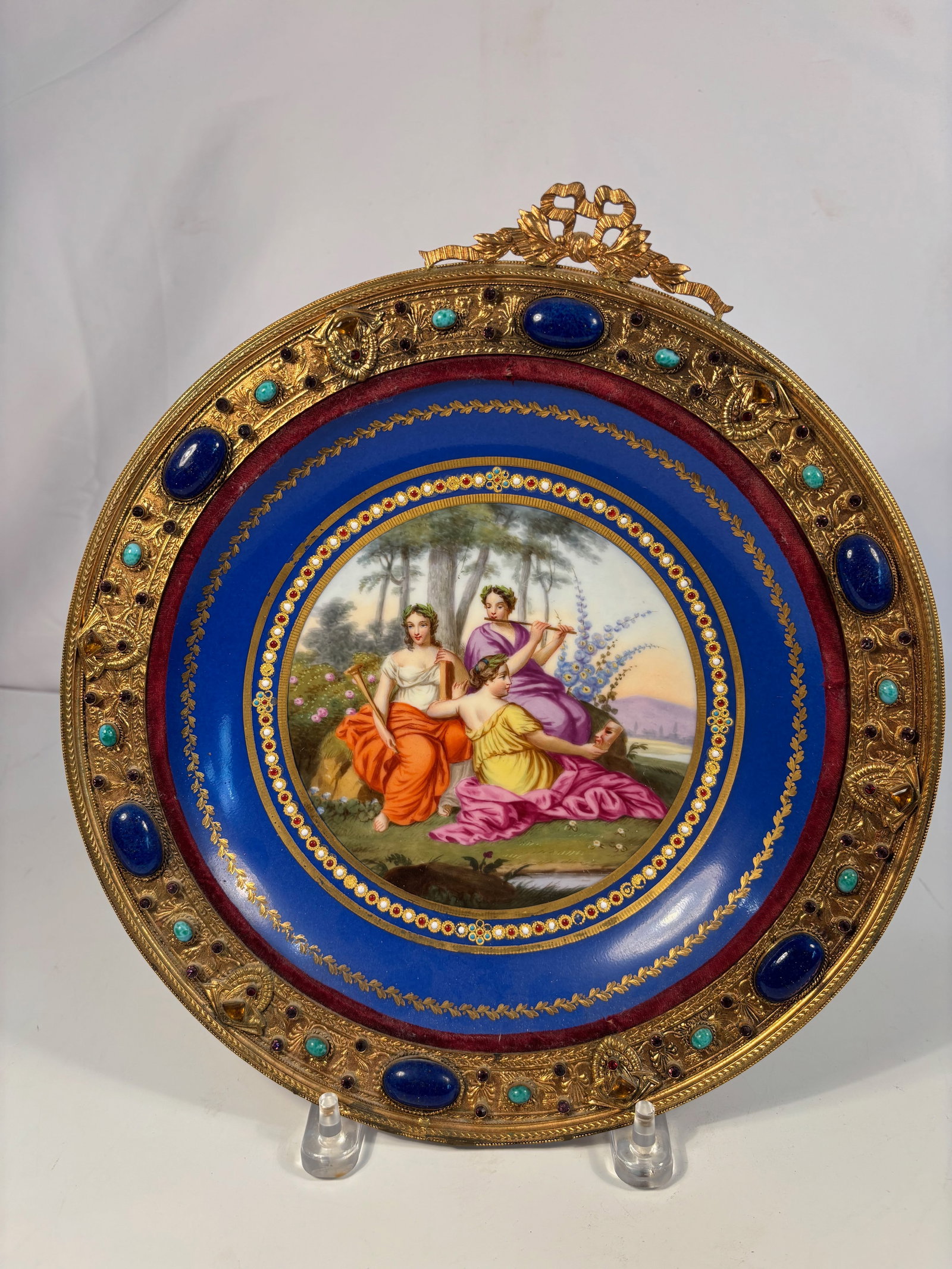 A Fine French Royal Blue Porcelain Plaque with Ormolu Jewelled Mount, Paris or Limoges, 19th Century: Circa 1850–1880; A finely painted French porcelain plaque, decorated with a neoclassical scene of three muses in a landscape, surrounded by a deep royal blue ground enriched with gilt jewelled borde