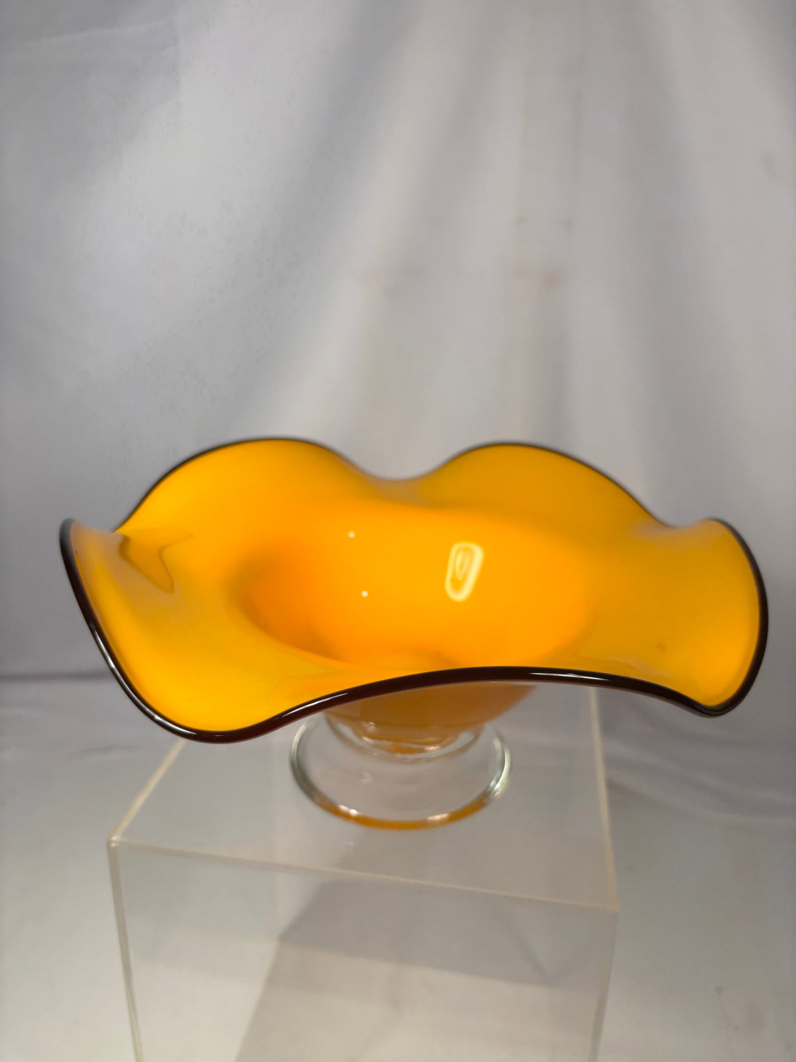 Vintage Hand Blown Orange Art Glass Pedestal Console Bowl: A striking hand-blown art glass centerpiece bowl featuring a vibrant orange finish with an elegant freeform ruffled rim. Raised on a clear circular pedestal foot, this sculptural bowl displays flowing