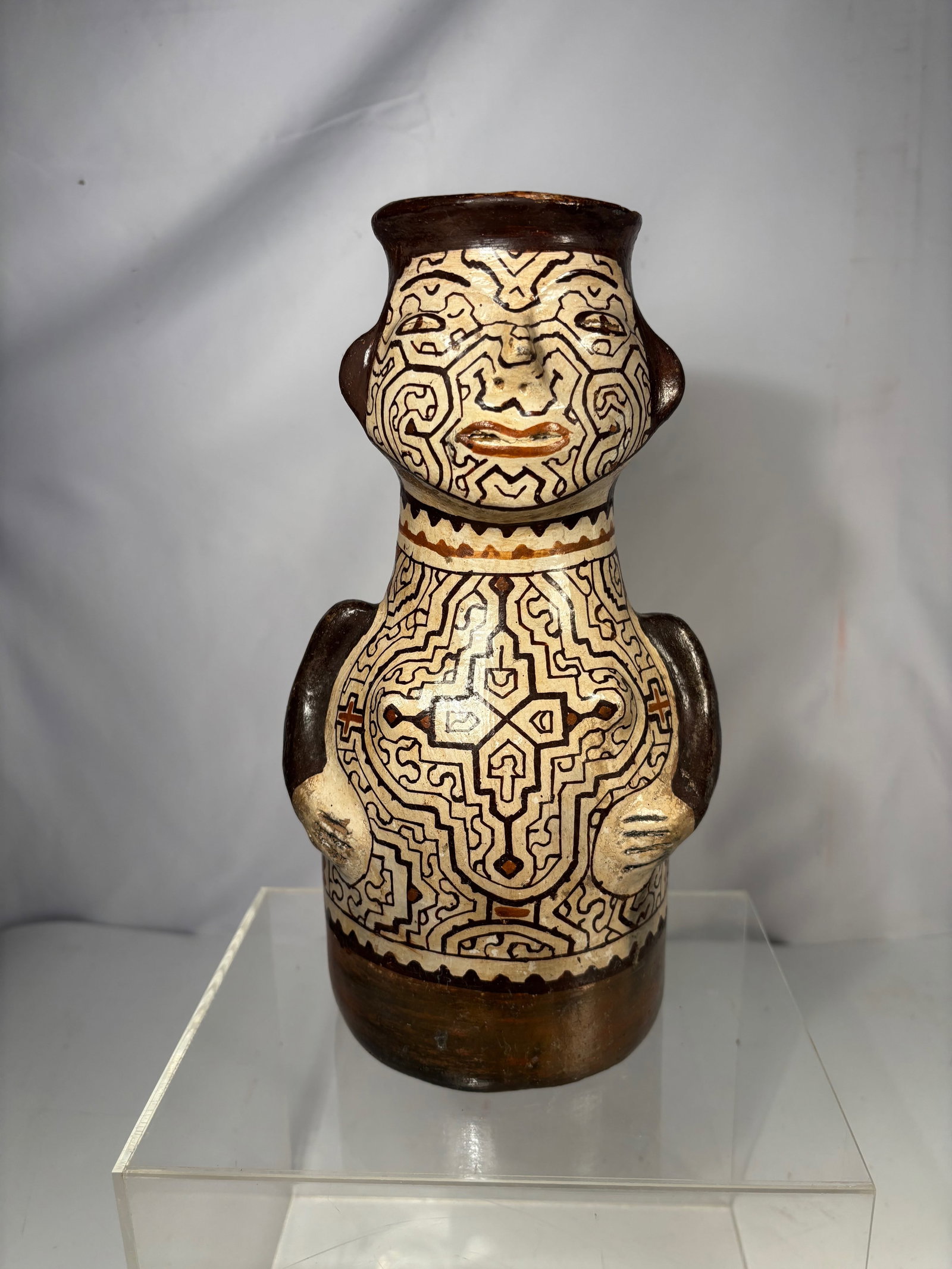 A Shipibo-Conibo Peruvian Pottery Figural Vase: Shipibo-Conibo Peruvian pottery figural vase, hand formed and decorated with intricate geometric labyrinth motifs in dark brown over a light ground. The vessel features a stylized human face with