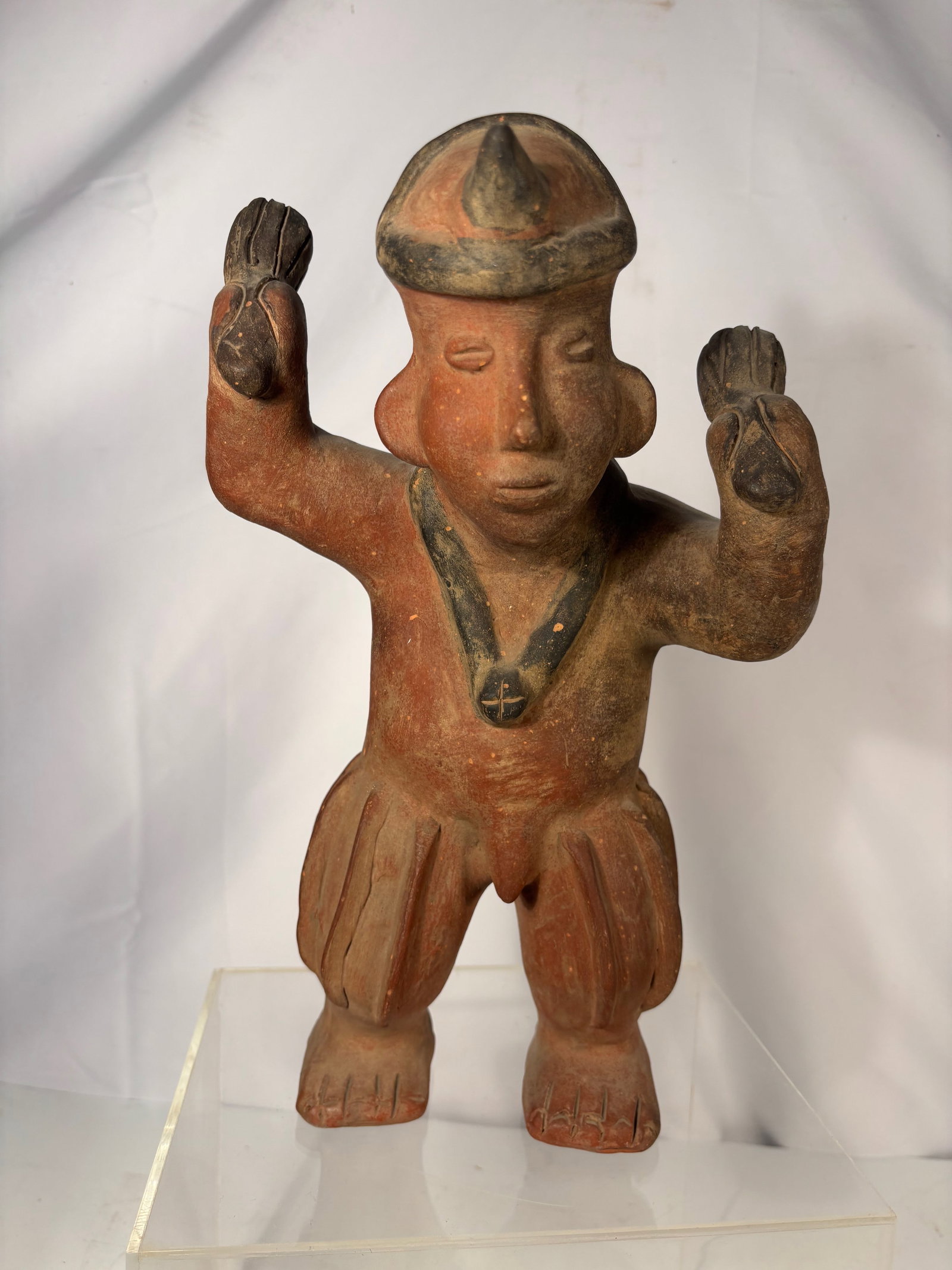 Pre-Columbian Style West Mexico Standing Figure: Pre-Columbian style ceramic standing figure, attributed to the West Mexico tradition. The figure is modeled with raised arms holding rounded objects, wearing a helmet-like headdress, necklace, and fla