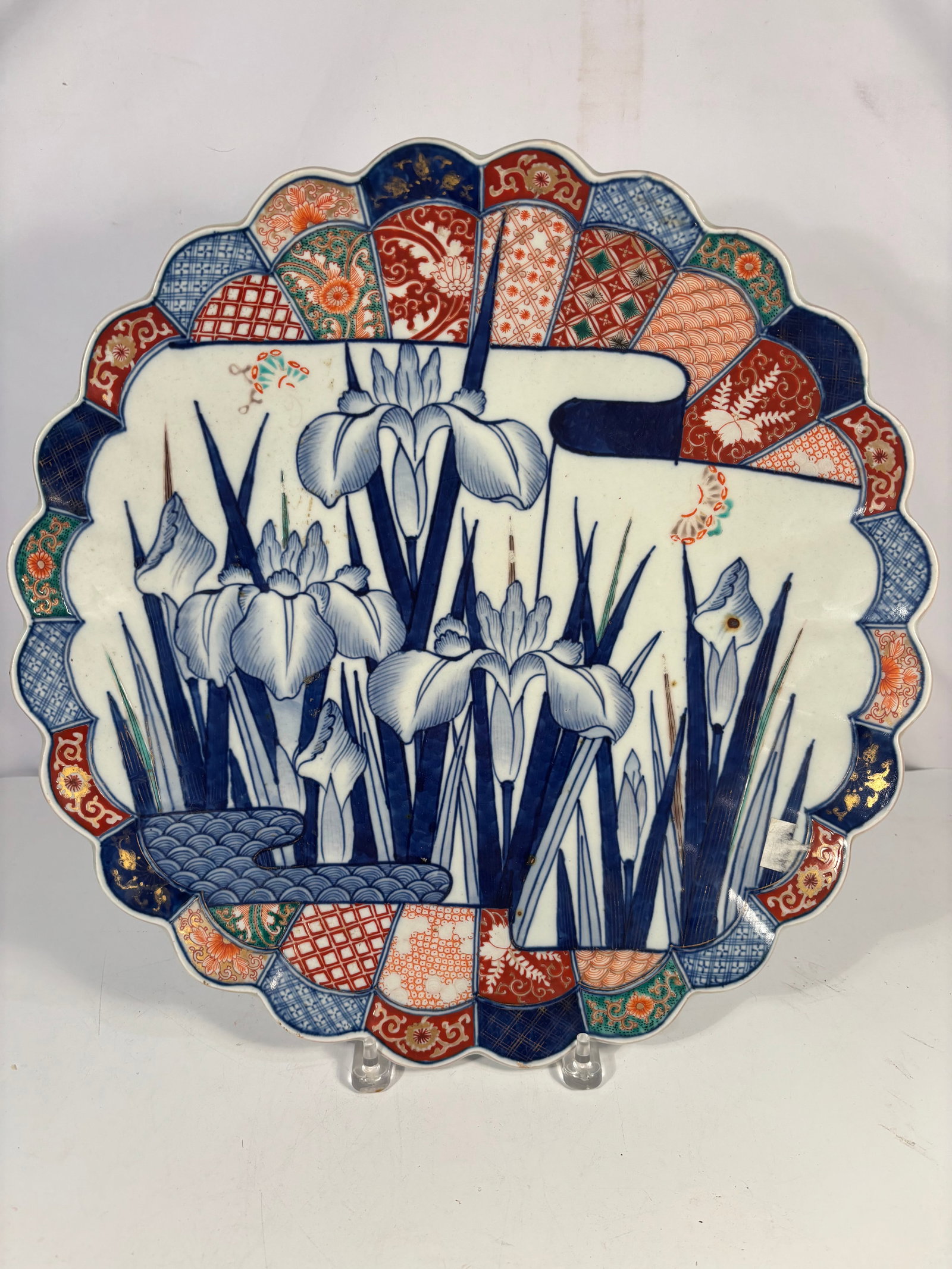 A Japanese Imari Arita Large Porcelain Charger, Iris Design, 17.5 In. Meiji Period (1868-1912): A large and finely hand-painted Japanese Imari porcelain charger, Meiji period, measuring 17.5 inches in diameter. The center features an elegant underglaze cobalt blue iris landscape above stylized w