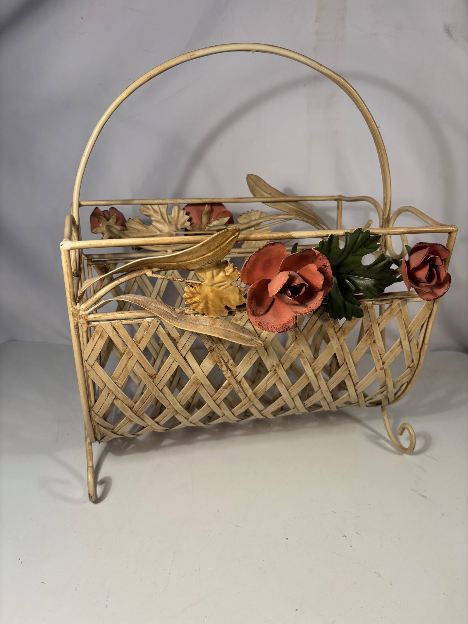 A Vintage Tole Floral Metal Basket Planter: Vintage decorative metal basket featuring gilt metal construction with applied floral decorations including roses and leaves. The basket has a lattice-form body with a curved handle and scrolled feet.