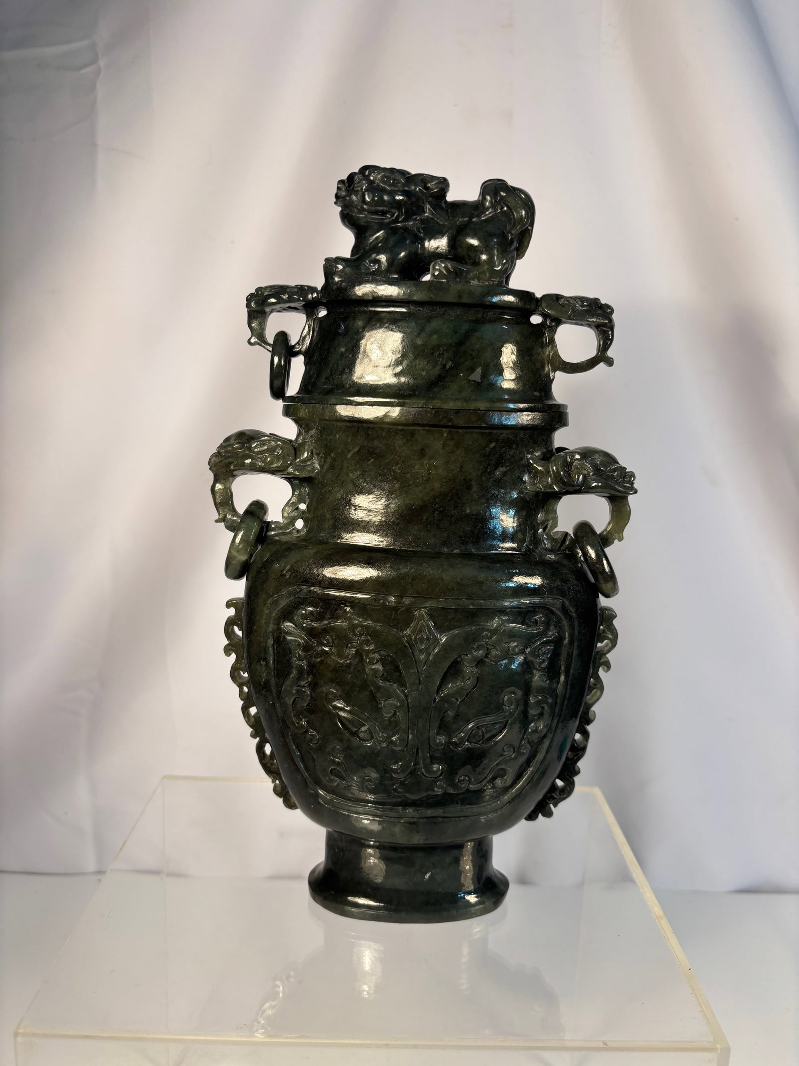 A Chinese Archaistic Carved Green Jade Covered Censer with Dragon Handles: A finely carved archaistic jade censer, the compressed ovoid body supported on a short circular foot, the sides decorated in shallow relief with stylized taotie mask and scroll motifs, flanked by a pa