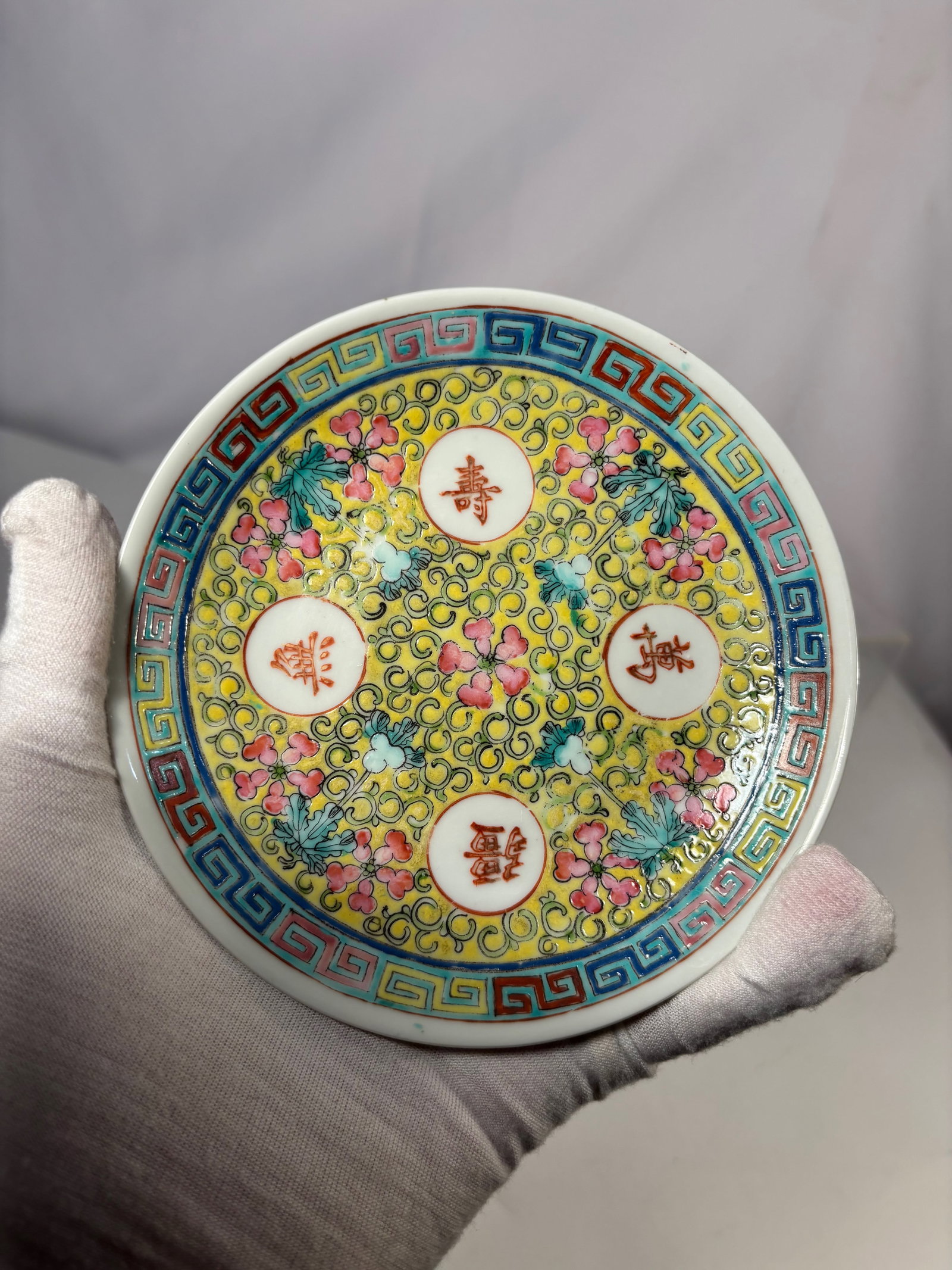 A Chinese Famille Rose Longevity Plate with Apocryphal Qianlong Mark: Chinese porcelain plate decorated in famille rose enamels on a vibrant yellow ground, featuring scrolling foliate motifs and floral designs. The center and interior are accented with roundels containi
