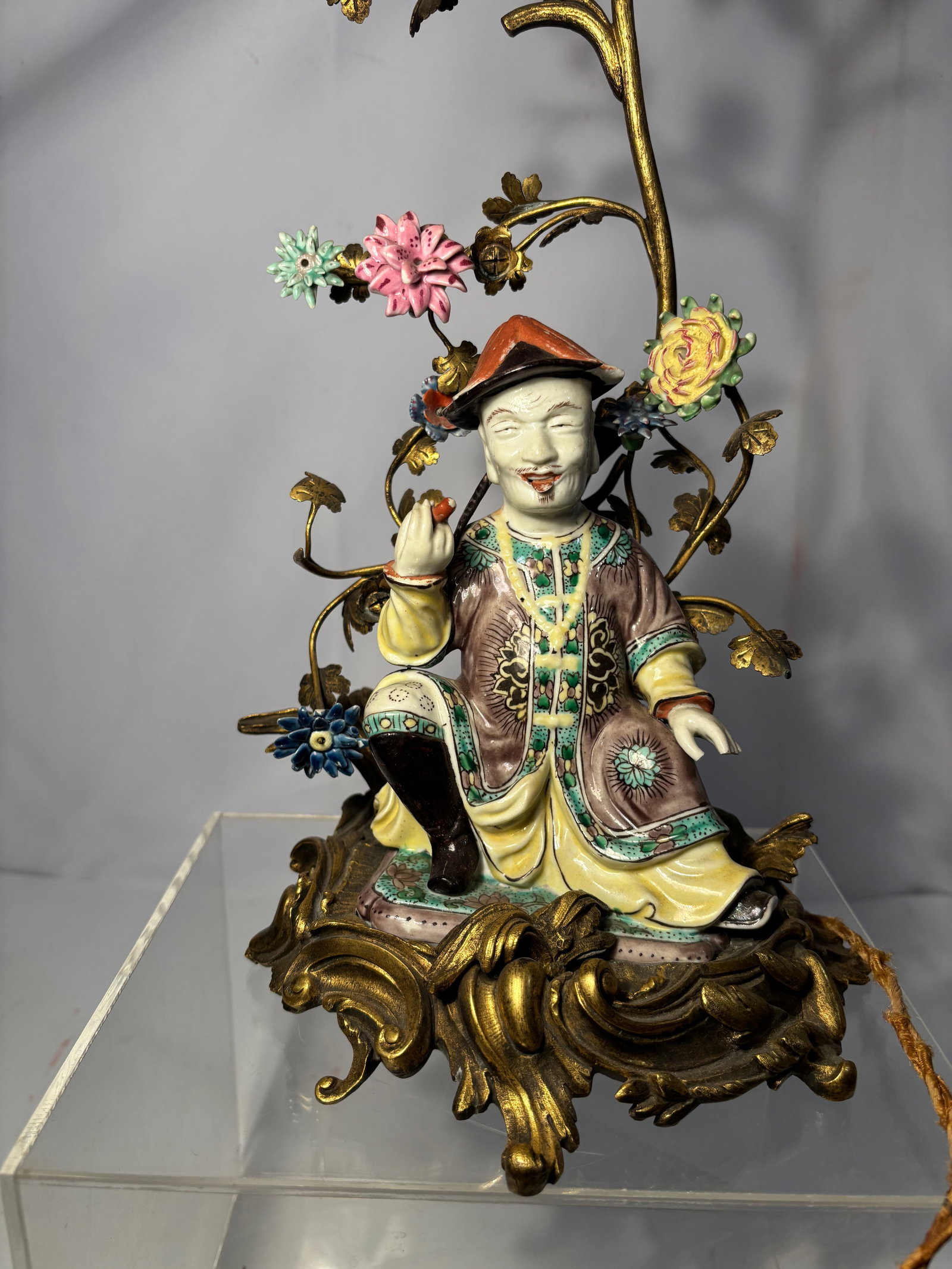 A Chinese Porcelain Immortal Figure in the 18th Century Style, Later European Gilt Metal Mount: Qing dynasty (1644-1912); Chinese porcelain figure depicting a seated male immortal, modeled in the 18th century style and decorated in famille-verte enamels of green, yellow, aubergine, and brown. Th