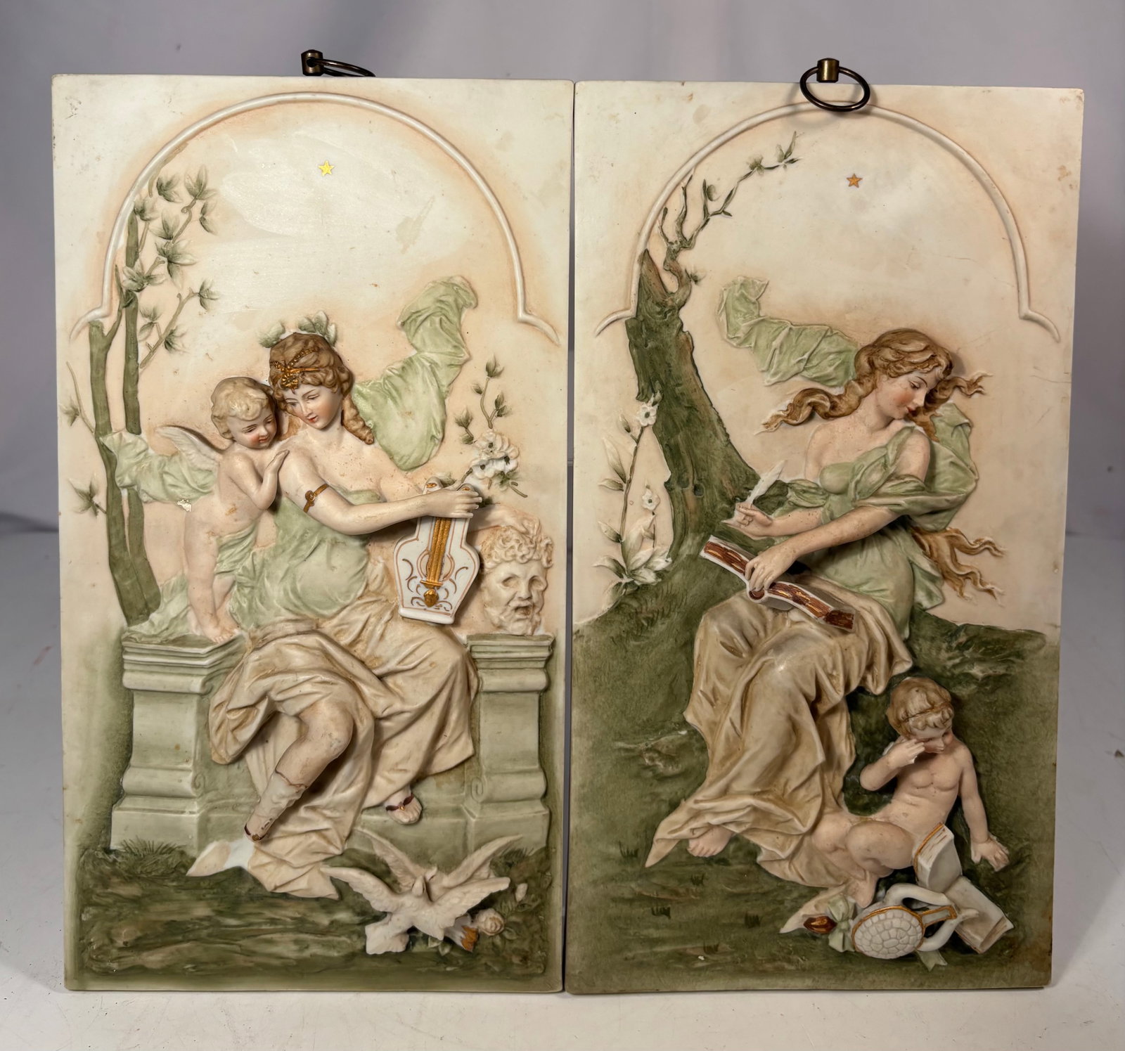 Pair of Mid-Century Arnart Creations Hand-Painted Porcelain Fairy and Cherub Wall Plaques, Japan: A charming pair of mid-century hand-painted porcelain wall plaques imported by Arnart Creations. Each rectangular plaque is finely modeled in high relief with a seated winged fairy accompanied by a ch