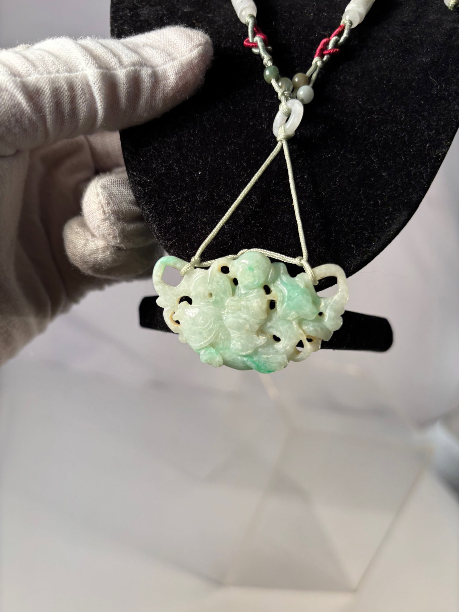 A Chinese Carved Jadeite Pendant Necklace: Necklace featuring a carved jadeite pendant depicting a decorative motif with openwork carving. The jade shows light green coloration with natural variations. Suspended from a cord necklace with adjus
