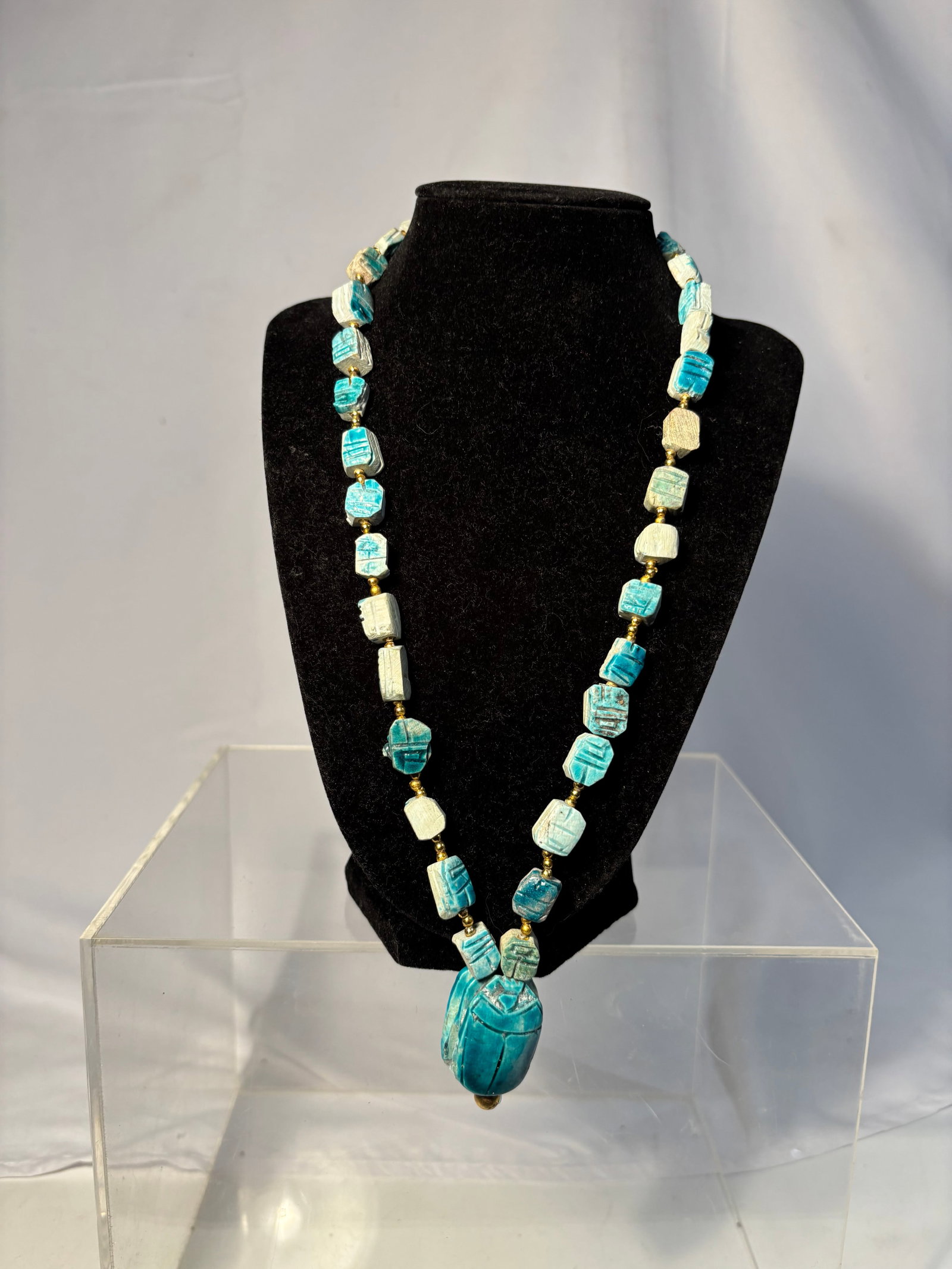 Vintage Egyptian Revival Faience Scarab Necklace: An Art Deco period Egyptian Revival necklace composed of carved scarab-form beads in turquoise blue and pale celadon tones, interspersed with gilt spacers and centered by a larger scarab pendant. Exec