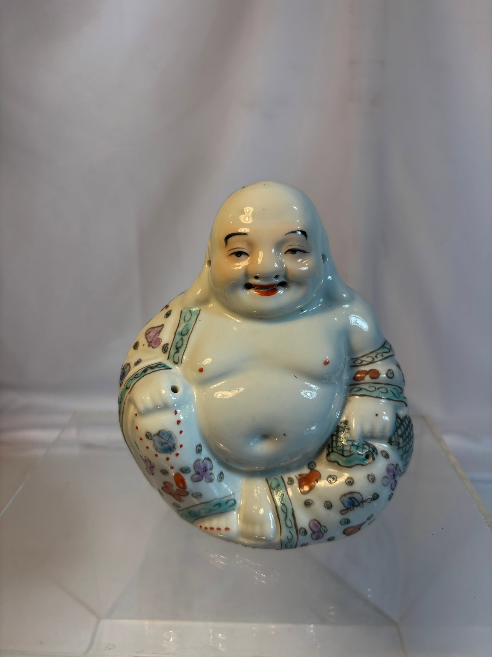 A Chinese Famille Rose Porcelain Laughing Buddha Figure: Early 20TH century, A Chinese porcelain figure depicting the Laughing Buddha (Budai), modeled seated with exposed belly and cheerful expression. Decorated in famille rose enamels with colorful floral 