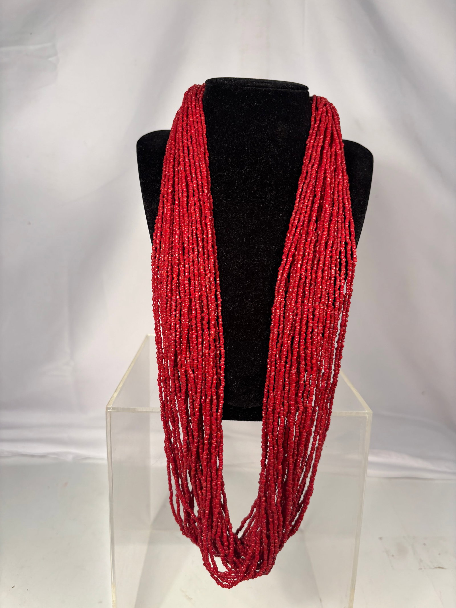 Long Multi-Strand Coral Bead Necklace, 30 Strands: Elegant multi-strand necklace composed of approximately 30 strands of coral-colored beads. The necklace features a decorative clasp with a cabochon coral accent. Rich orange-red coloration and impress