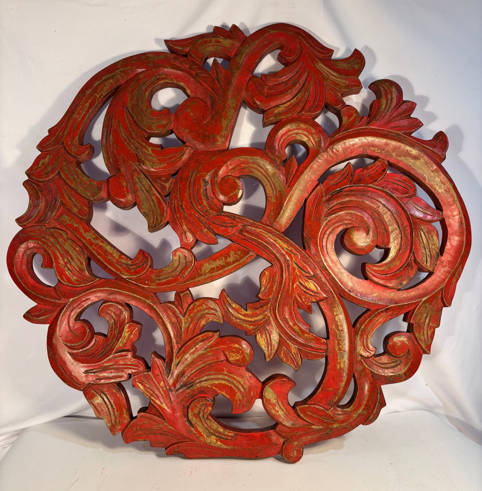 Large Indian Carved and Gilt Wood Openwork Wall Panel, 30 Inches: A large circular carved wood wall panel featuring an elaborate openwork design of scrolling acanthus leaves and foliate motifs. Finished in deep red with distressed gilt highlights, creating an ornate