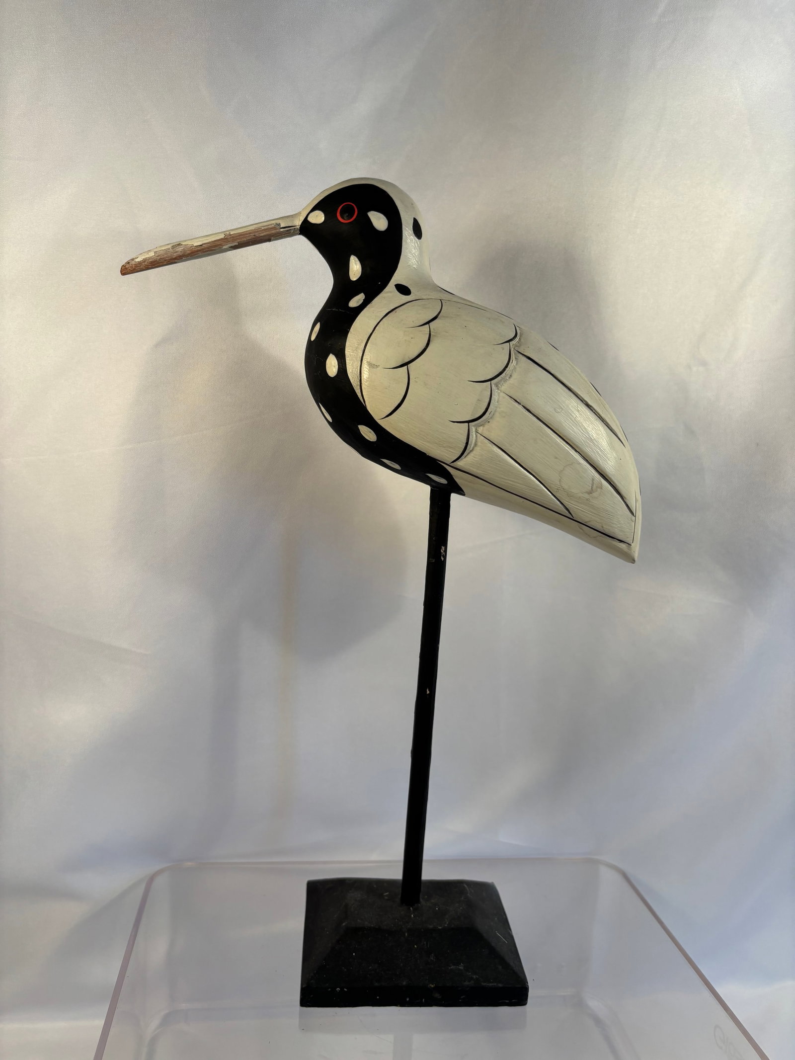 Folk Art Carved and Painted Spotted Shorebird Sculpture on Stand: Decorative folk-art shorebird sculpture featuring an elongated bill, stylized black-and-cream spotted plumage, carved wing details, red-ringed eyes, and long legs mounted on a rectangular black base. 