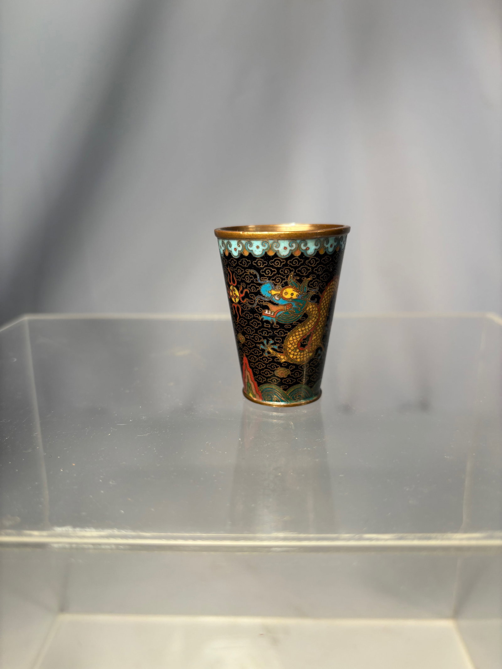 A Chinese Cloisonné Enamel Cup with Dragon Design: Qing dyansty(1644-1912); Of tapering form with slightly flared rim, finely decorated in multicolored enamels with a five-clawed dragon pursuing a flaming pearl among ruyi-shaped clouds, all reserved o