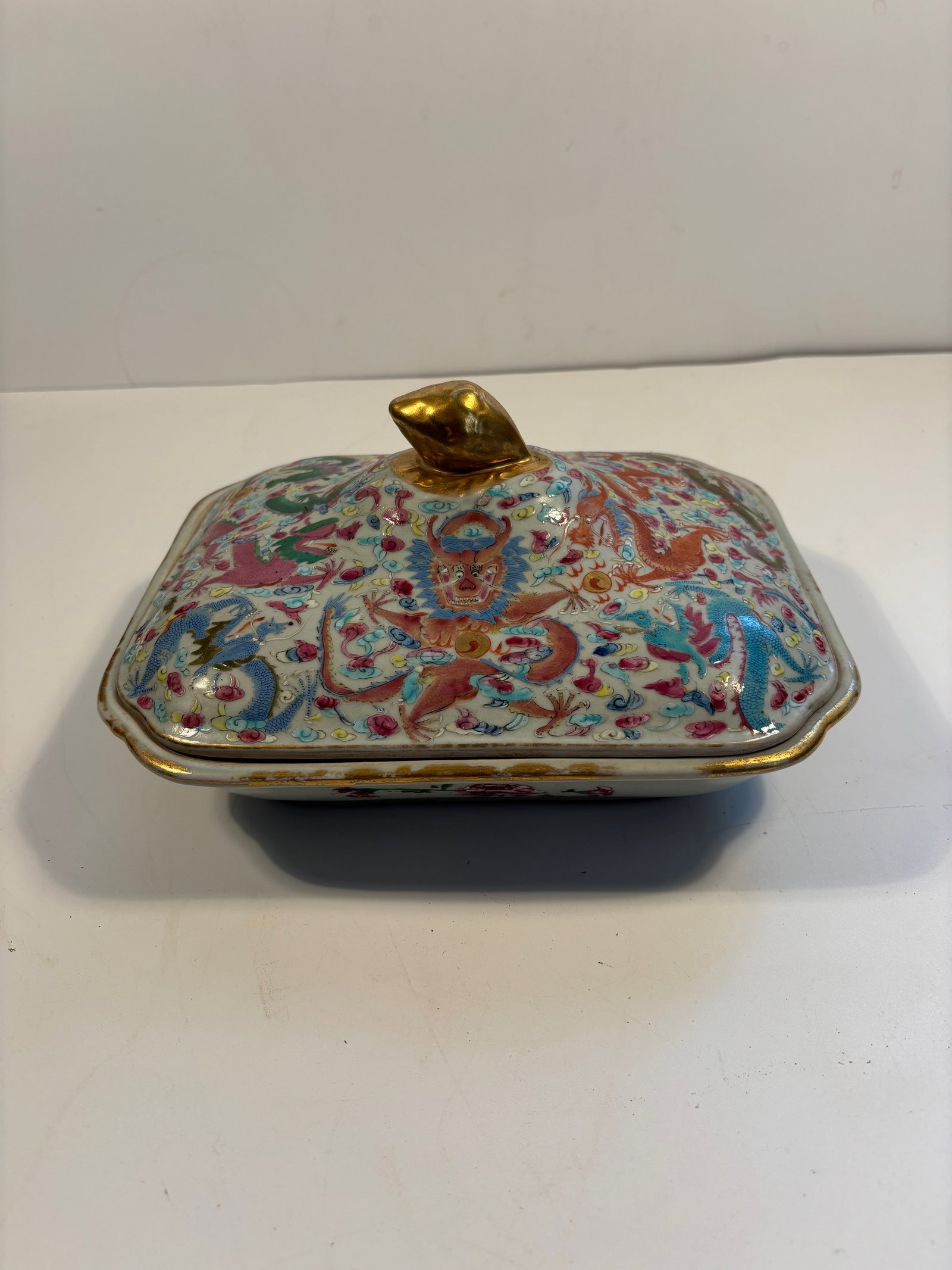 A Chinese famille rose porcelain covered box: Qing Dynasty (1644-1912), The design features five-clawed imperial dragons amidst clouds and flames. The bright pinks, blues, purples, and golds suggest famille rose enamel; The gold-glazed finial on 