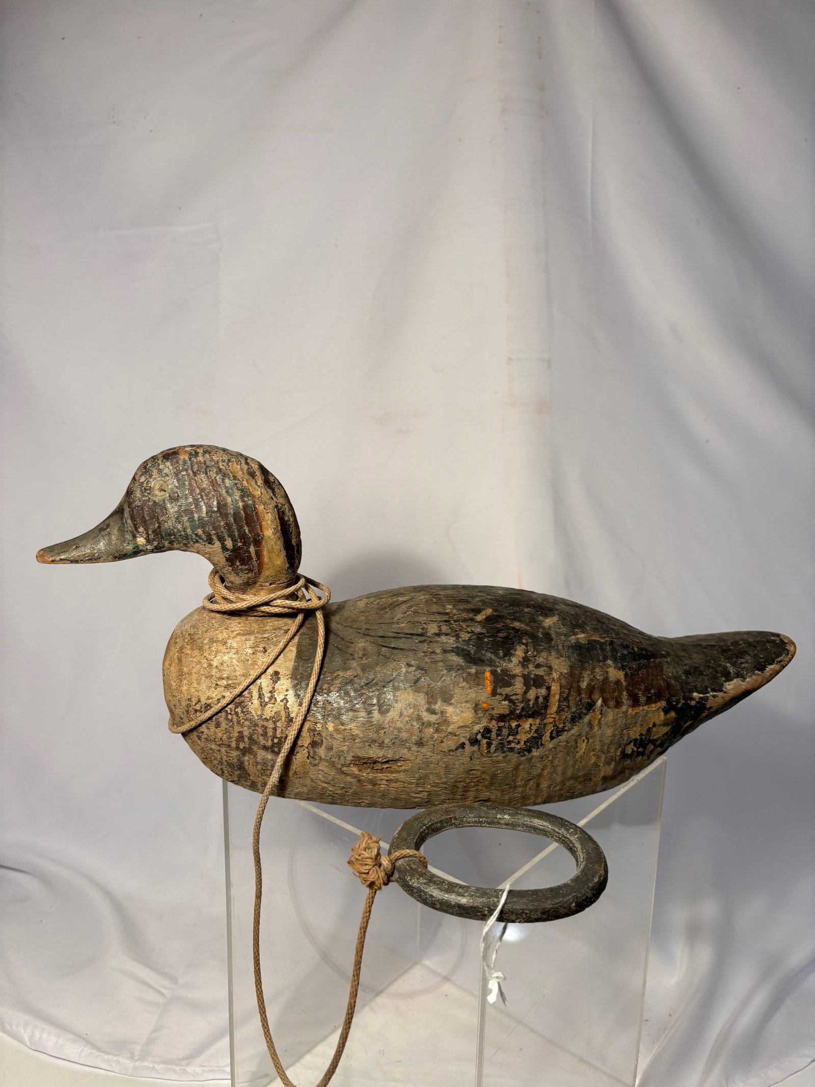 An Early 20th Century “L. Hancock?? Carved Wooden Duck Decoy: Early 20th century hand-carved wooden duck decoy bearing carved “L. Hancock” mark to the weight strap. Retaining heavily worn original painted surface, old rigging, and attached circular weigh