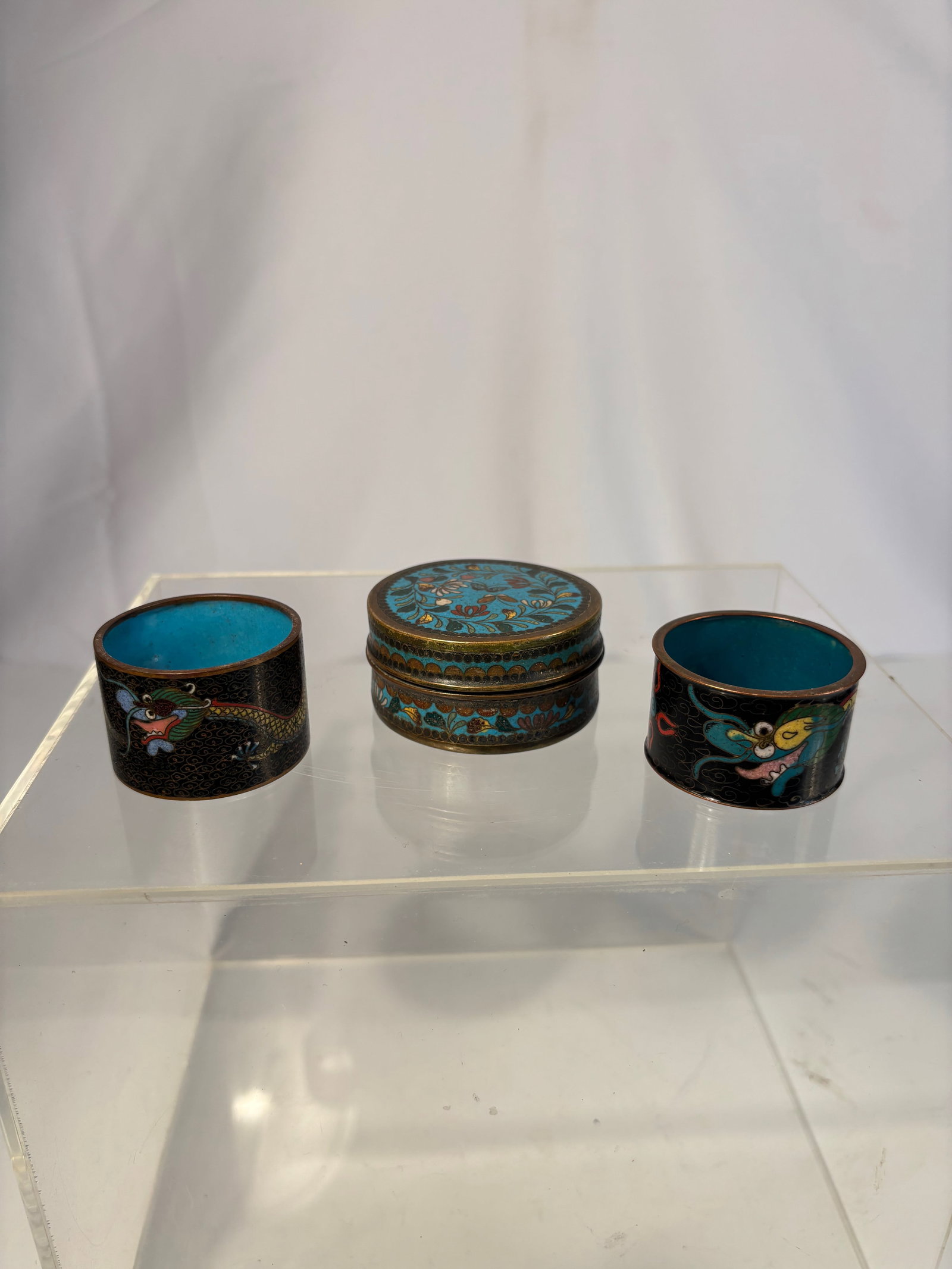 Set of 3 Vintage Chinese Cloisonné Enamel Pieces – Dragon & Floral Designs: A charming set of three vintage Chinese cloisonné enamel pieces, including two napkin rings and one small lidded box. Each piece is crafted on a brass base and decorated with colorful enamel designs 