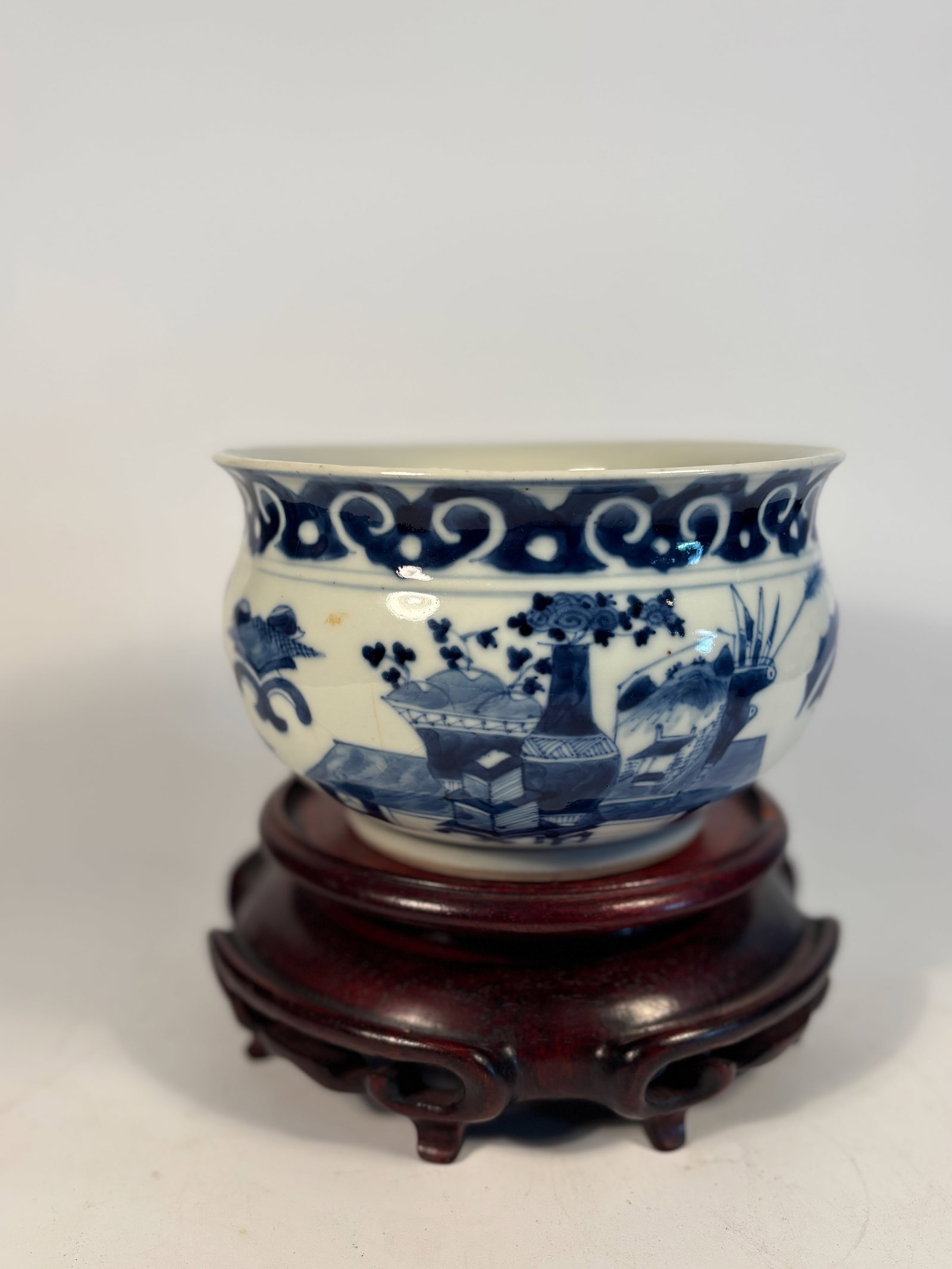 A Chinese Blue and White Porcelain jar with Scholar’s Objects: Kangxi period (circa 1700–1722), finely decorated in underglaze cobalt with a continuous scene of scholar’s objects (bogu), including stacked books, incense burners, vases, and flowering branches 