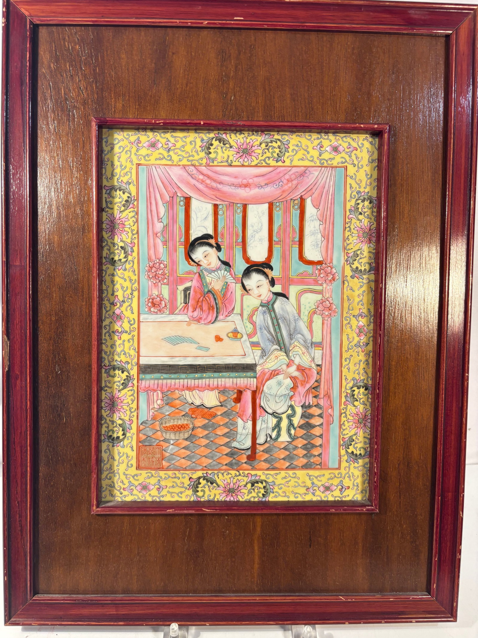 Chinese Famille Rose Porcelain Plaque Depicting Court Ladies: A Chinese famille rose porcelain plaque finely enameled with two elegant court ladies in a richly decorated interior. One woman holds a round fan while the other sits beside a table with writing mater