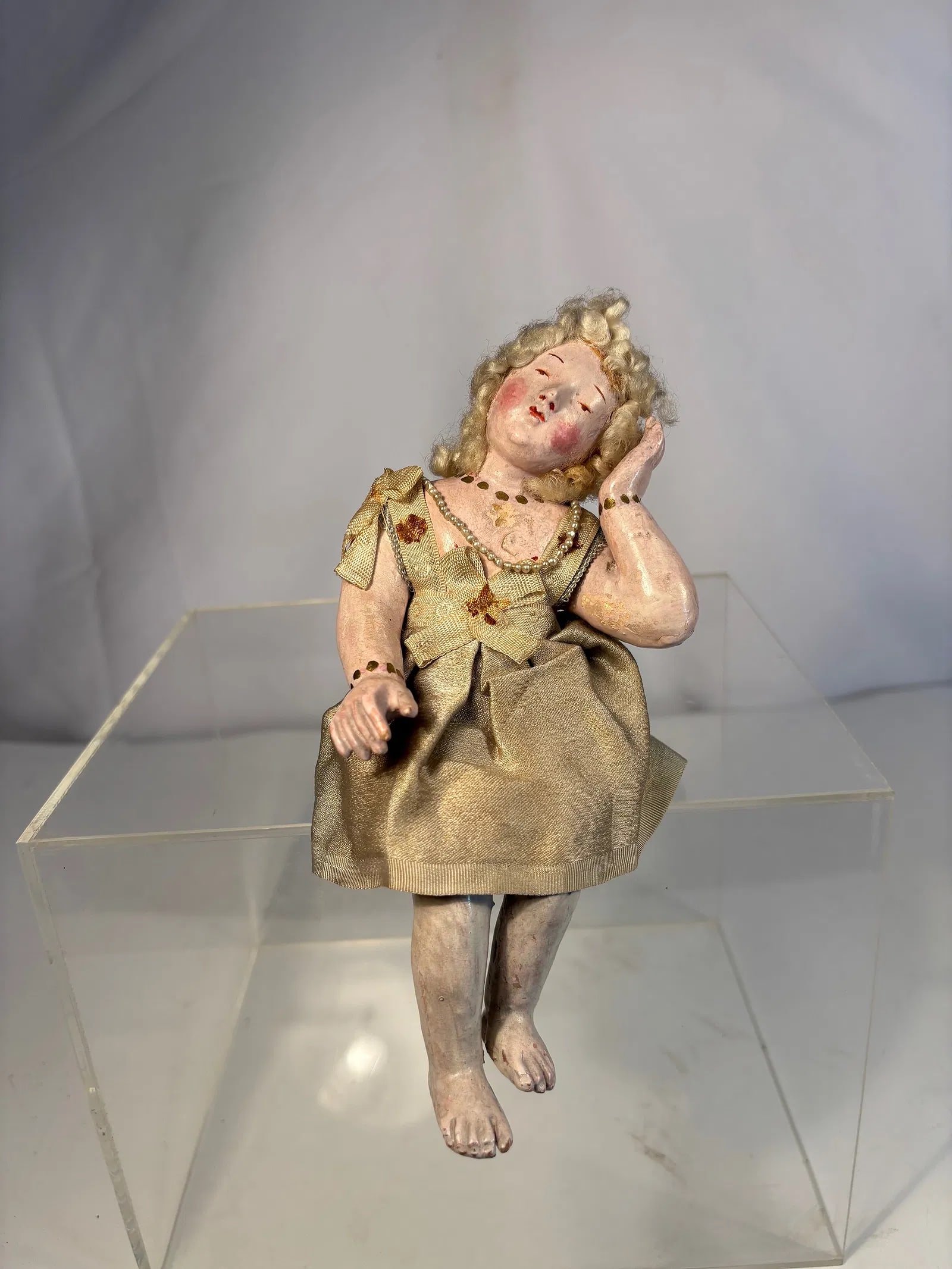 Neapolitan Polychrome Terracotta and Gesso Figure of a Seated Girl, 18th Century: Finely modeled figure depicting a young kid in a contemplative pose, with delicately painted features, a applied wool hair arranged in curls. Dressed in a period silk gown with ribbon and bead decorat