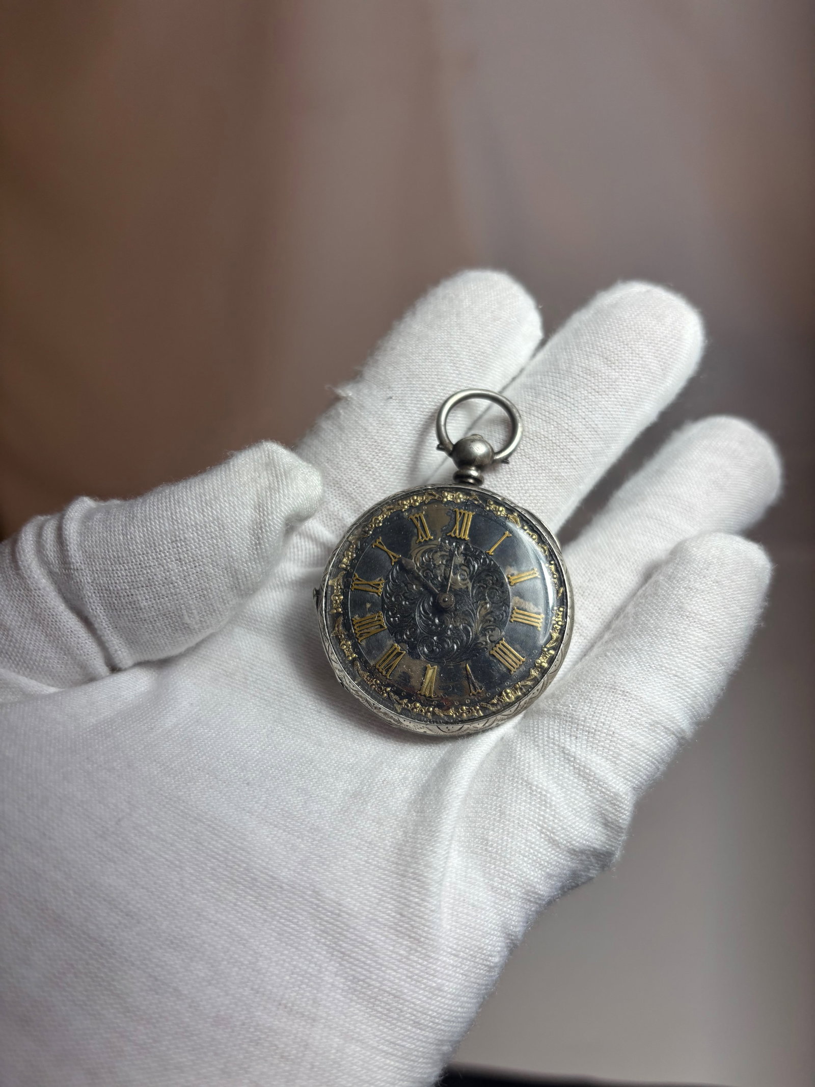 Antique Style Pendant Pocket Watch with Black Dial: Antique pendant-form pocket watch featuring a black dial with gilt Roman numerals in an engraved silver-tone case. Decorated reverse cover with scrolling motifs. Appears early 20th century in style. F