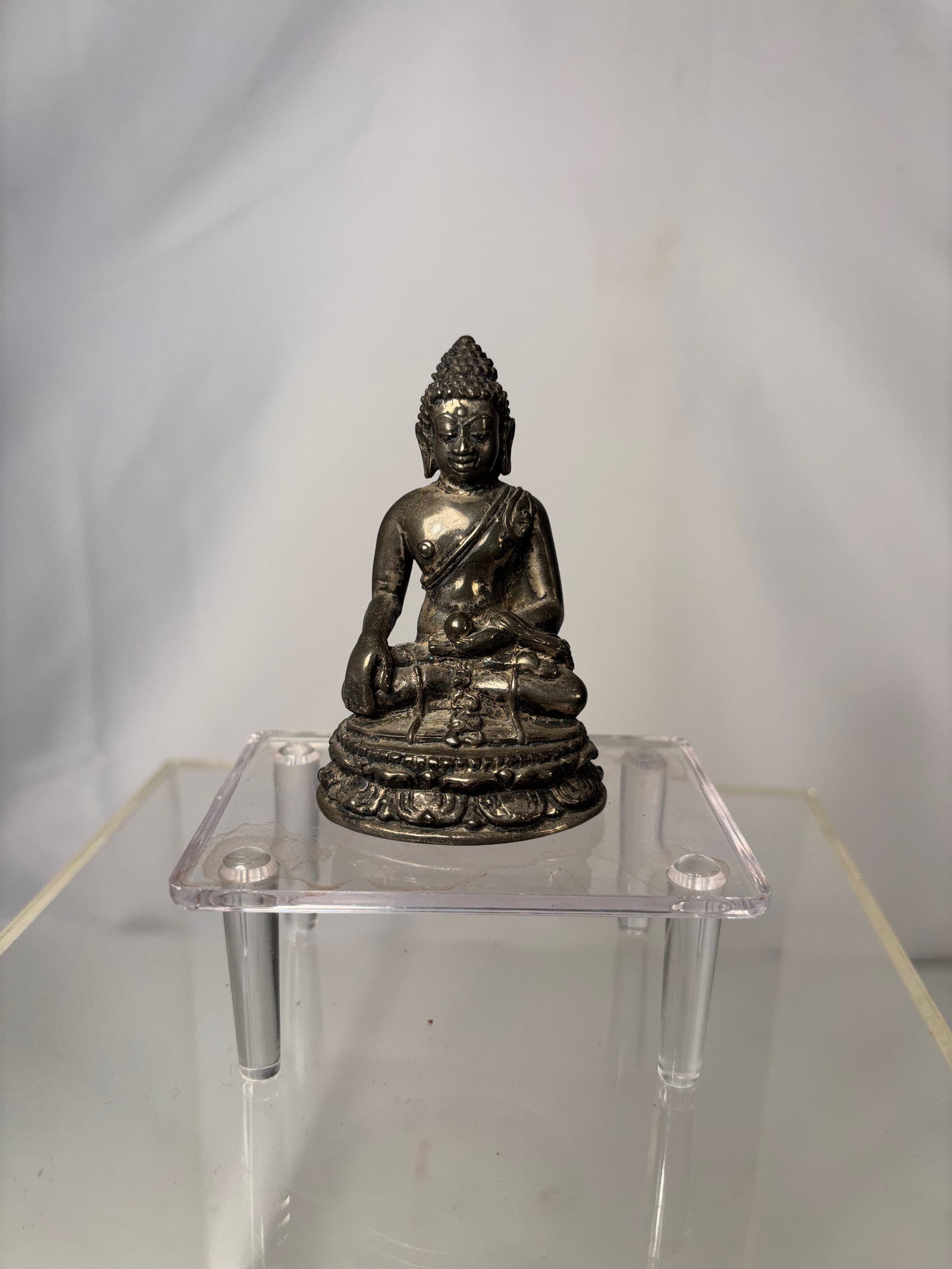 A Small Chinese-Silver Seated Buddha Figure: 19th century, Small cast metal figure depicting a seated Buddha in a meditative pose, resting on a lotus-form base with detailed relief decoration. The figure features a serene facial expression, text