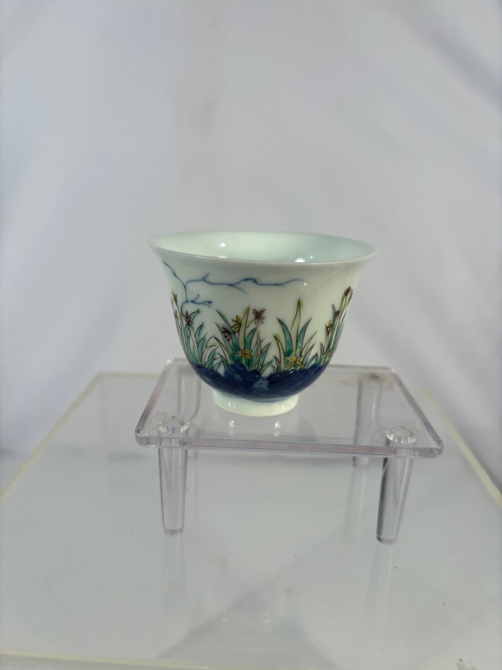 A Chinese Famille Rose Porcelain Cup, Kangxi Mark: 20th century; A Chinese porcelain cup decorated in famille rose enamels, finely painted with floral and garden motifs against a white ground. The base bears a blue six-character Kangxi mark reading ��