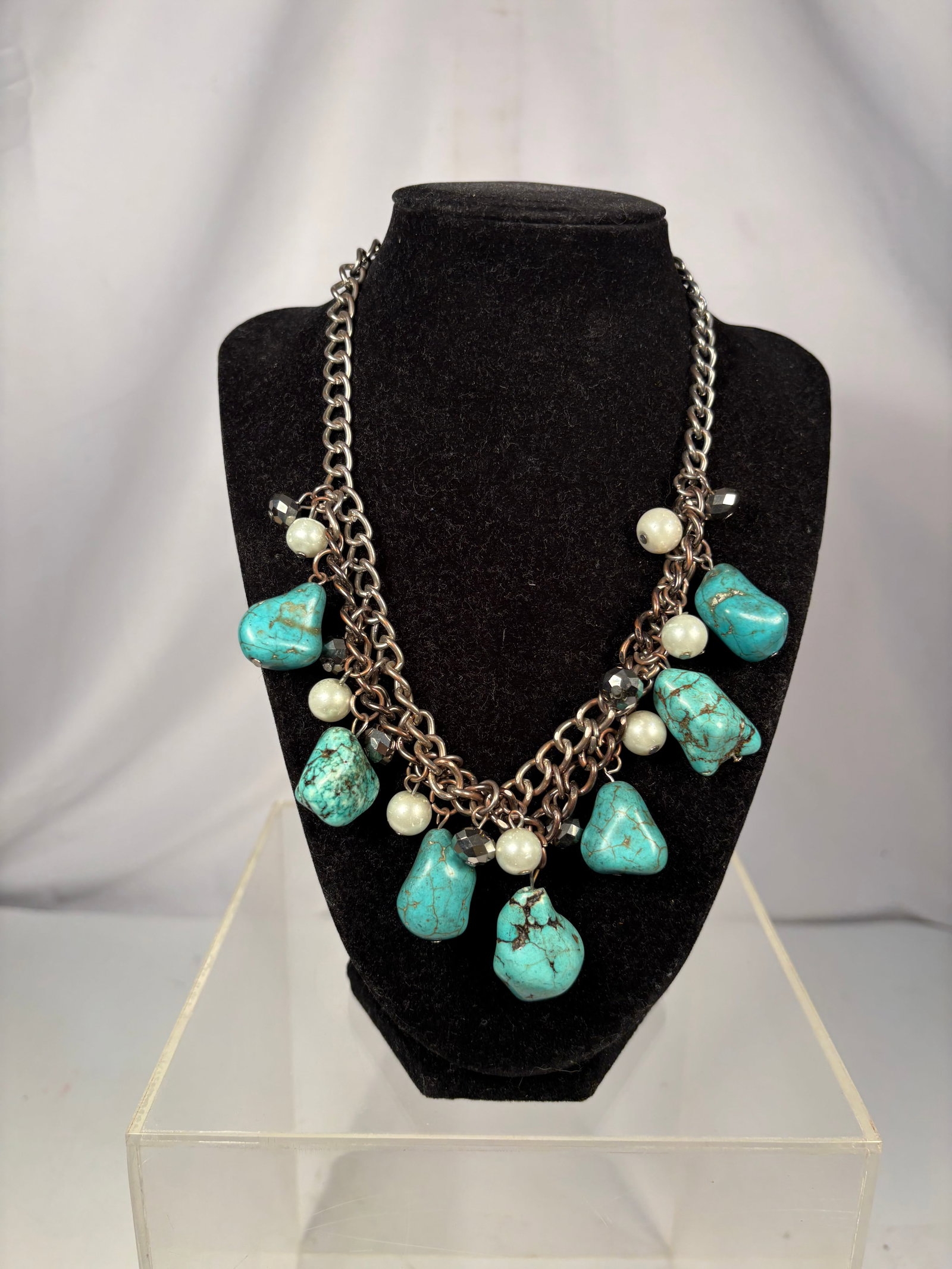 Vintage Turquoise Nugget and Pearl Multi-Chain Charm Necklace: A vintage statement necklace featuring multiple gunmetal-tone chains decorated with turquoise nugget drops, pearl beads, and faceted crystal accents. Finished with a lobster clasp and adjustable exten