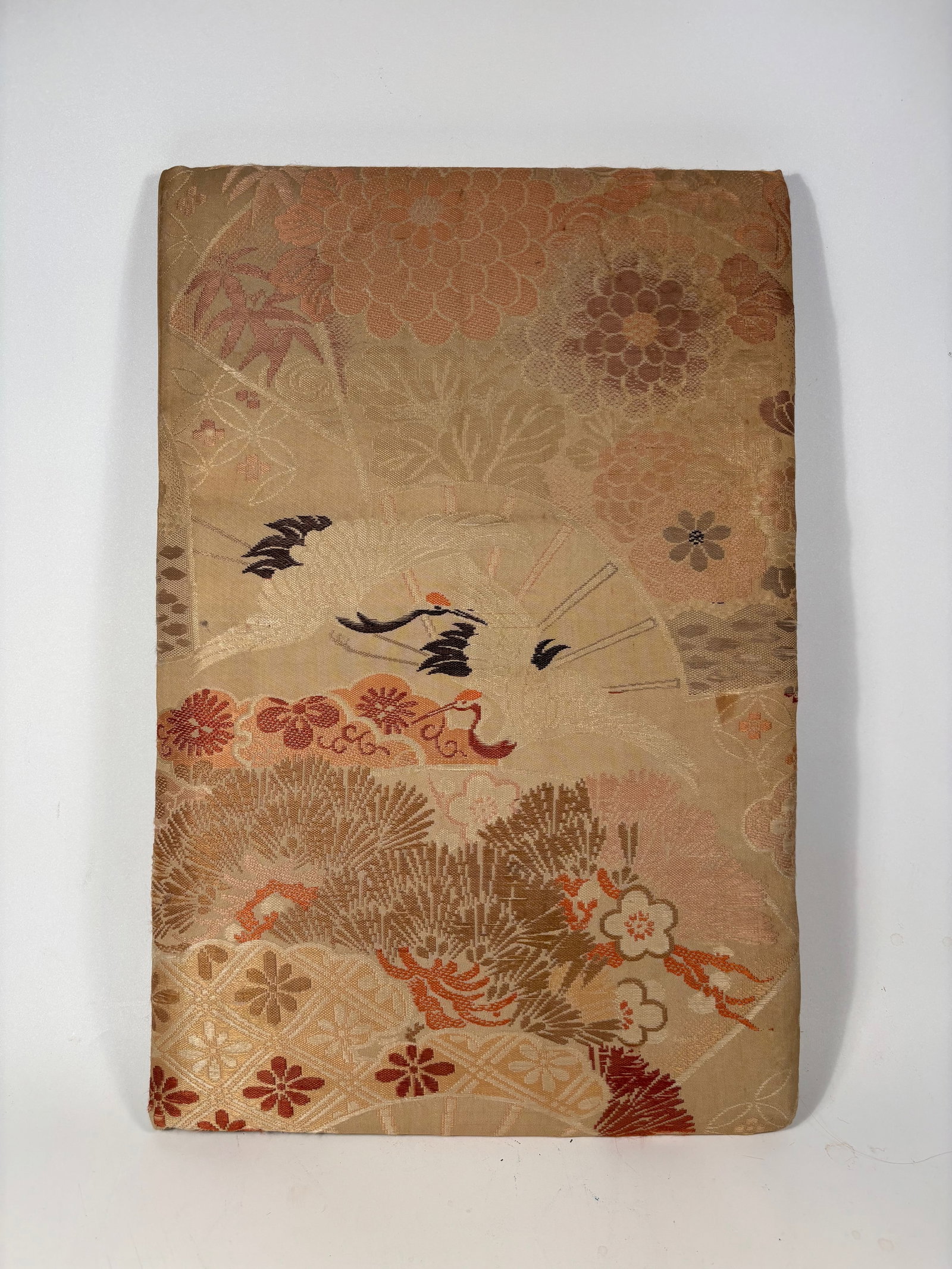 A Japanese Textile-Covered Album with Crane & Floral Motifs – Silk Brocade Cover: 19th Century; A vintage Japanese folding book or photo album, covered in elegant silk brocade fabric featuring a detailed and symbolic design of flying cranes among chrysanthemums, plum blossoms, and 
