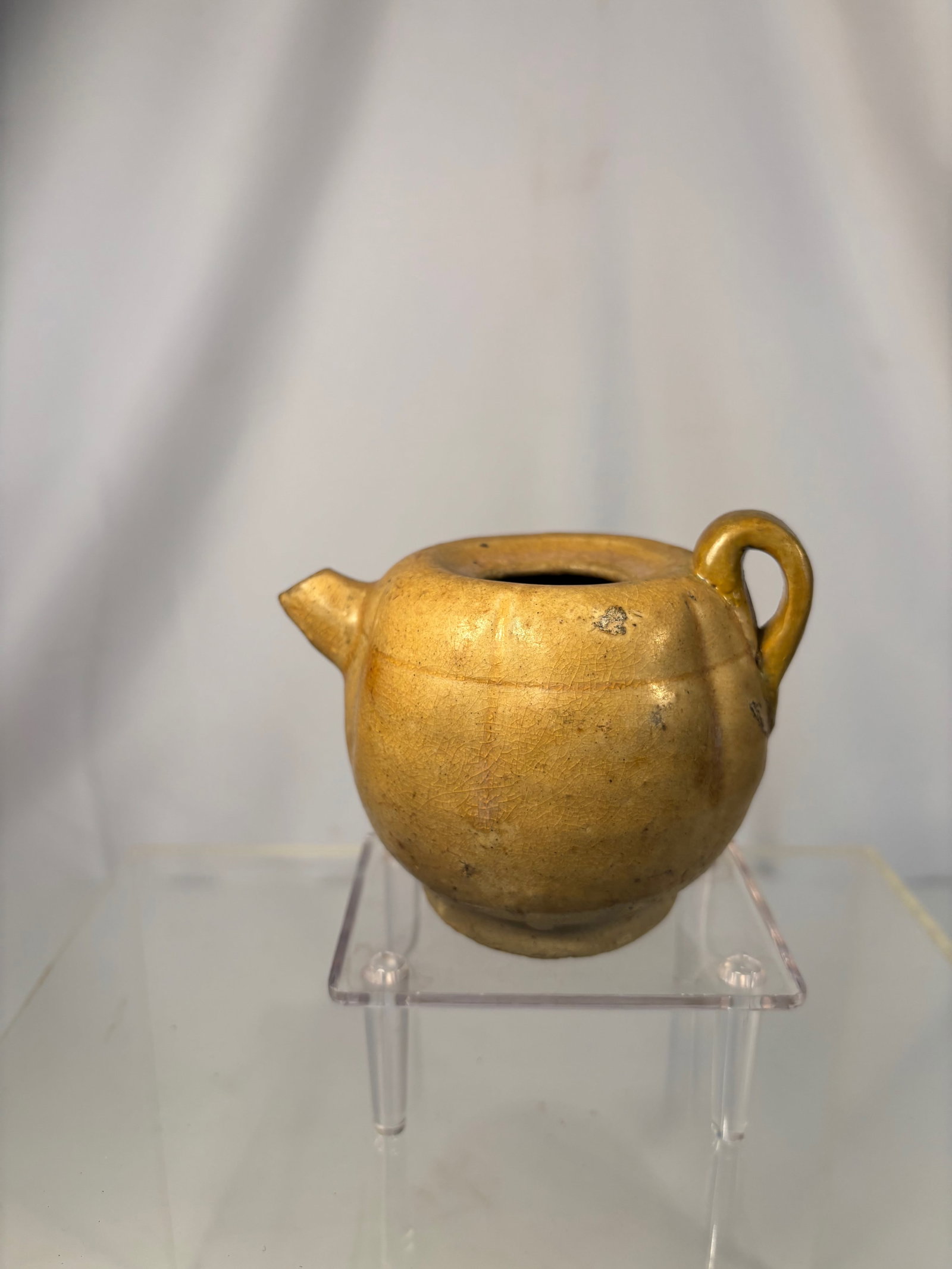 A Chinese Tang Dynasty Yellow-Glazed Stoneware Water Dropper, circa 8th–9th Century CE: Of rounded globular form with a short spout and loop handle, the vessel is covered overall in a lustrous amber-yellow lead glaze stopping neatly above the foot to reveal the buff-colored stoneware bod