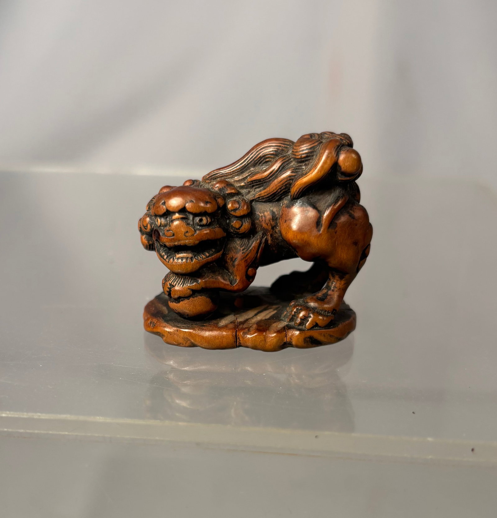 Japanese Wood Shishi Netsuke, Signed Hojitsu: By Meikeisai Hojitsu, signed Hojitsu Japan, Edo (Tokyo), mid-19th century, Edo period (1615-1868); Finely carved as a powerful shishi standing with one forepaw resting upon a ball, its head lowered an