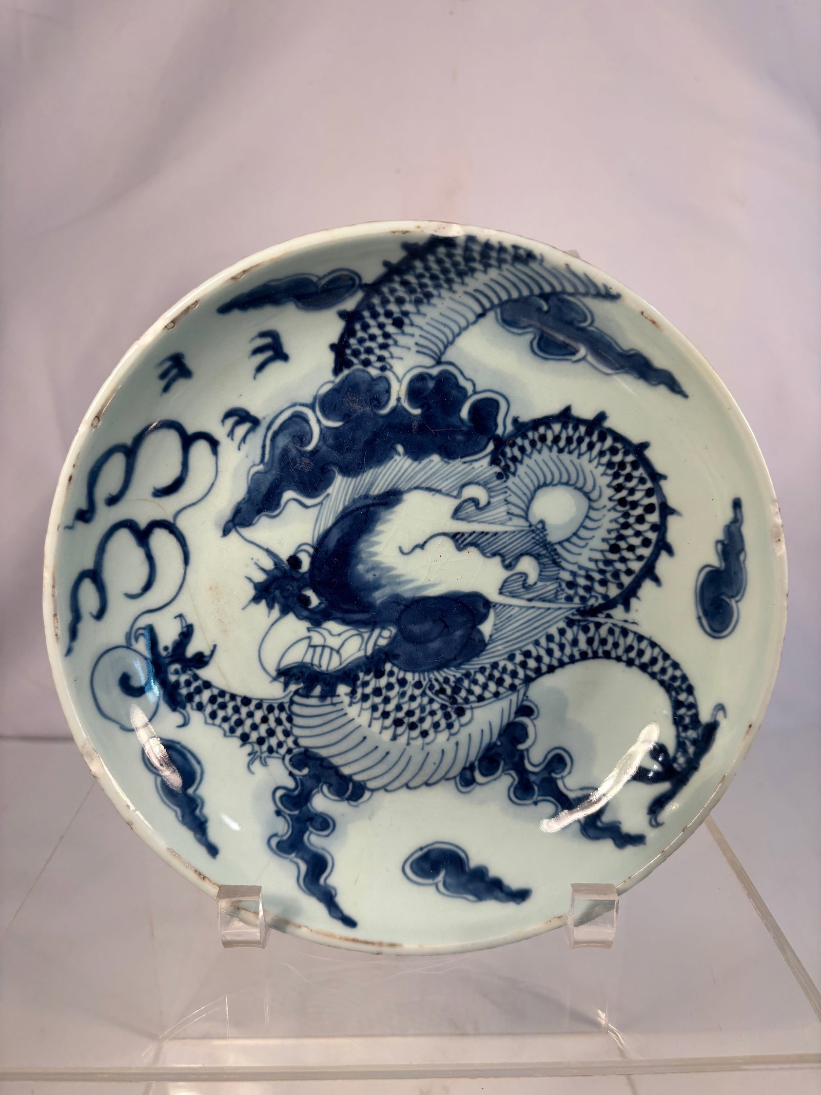 A Chinese Blue and White Porcelain Dragon Dish, Yongzheng period (1723–1735): The shallow rounded sides rising from a neatly cut foot to a slightly everted rim, finely painted in vibrant cobalt blue with a five-clawed dragon writhing among ruyi-shaped clouds, chasing a flaming 