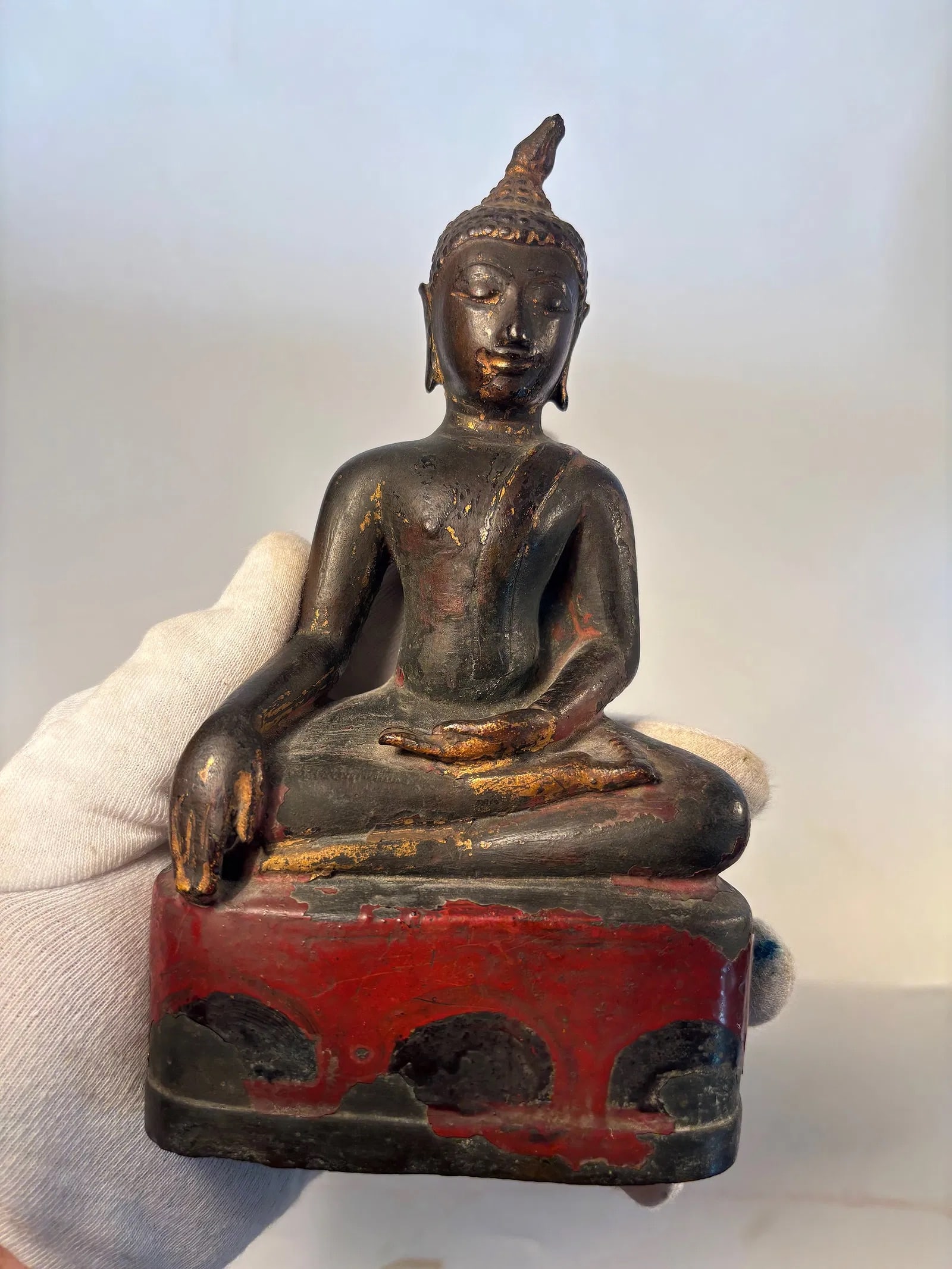An asian seated bronze buddha statue: 17th century to 18th century ; The Buddha is seated in dhyana (meditation) with one hand in the earth-touching gesture, symbolizing the moment of enlightenment. Traces of original gilt and red lacquer