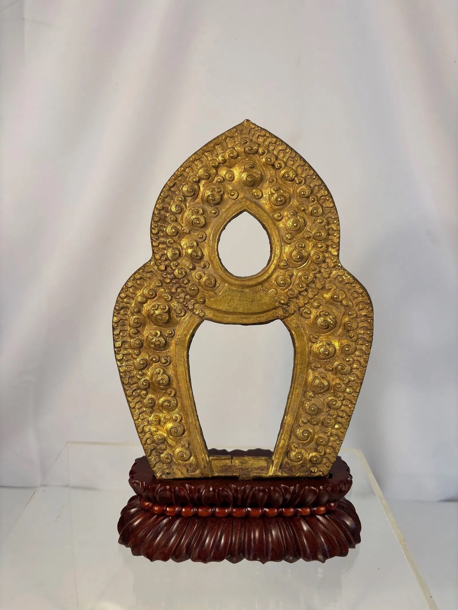 Gilt-Bronze Buddhist Aureole (Flame Mandorla) on Wood Stand , Tibet or Nepal, 18th–19th century: A finely cast gilt-bronze Buddhist aureole, the teardrop form richly decorated with rows of swirling flame and lotus motifs in high relief, representing the radiance of enlightenment. The back shows a