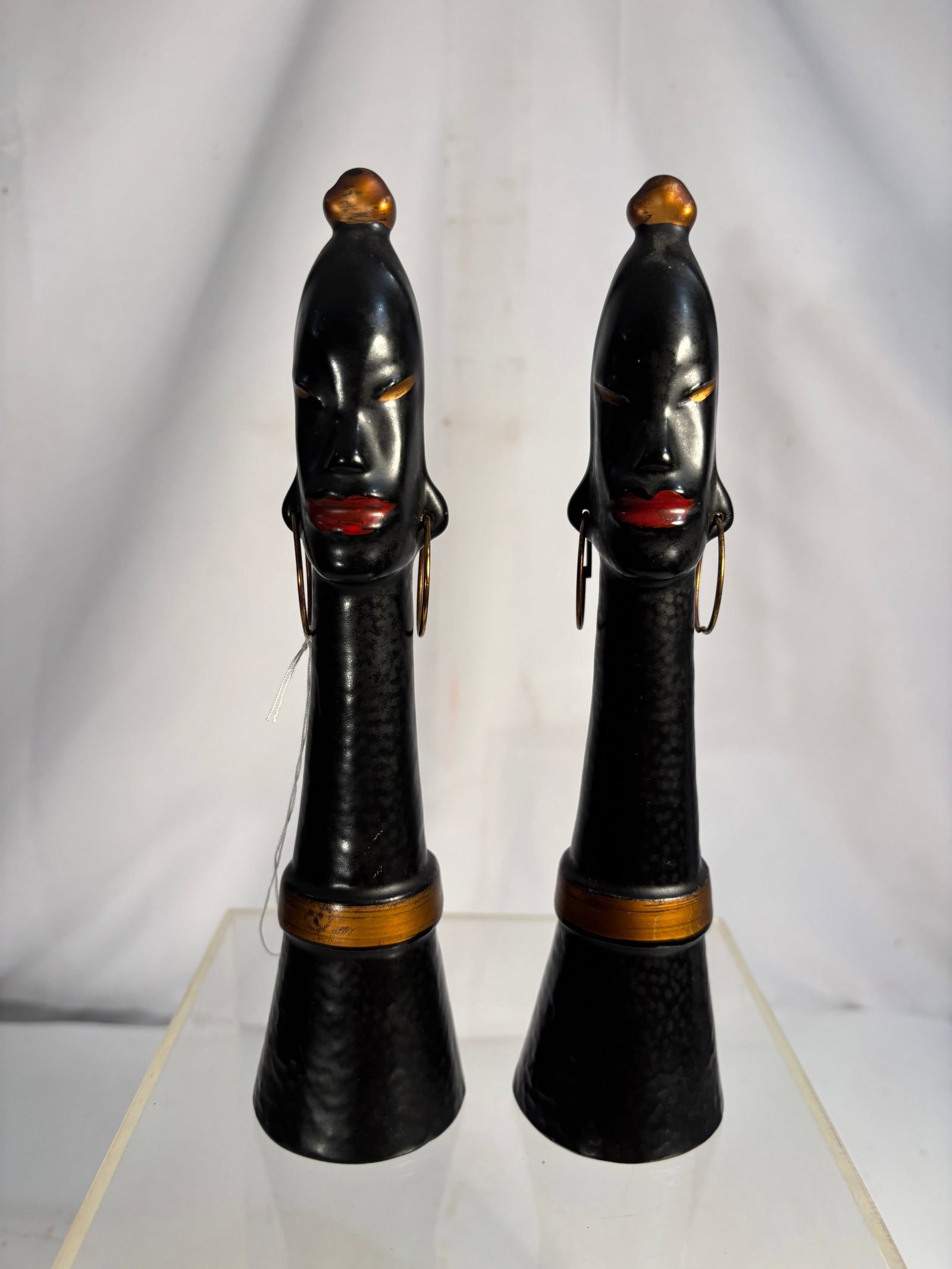 Pair of Vintage Porcelain African Woman Figural Salt and Pepper Shakers: A pair of vintage porcelain salt and pepper shakers modeled as stylized African women with elongated necks and expressive facial features. Each figure is finished in glossy black with red lips and gol